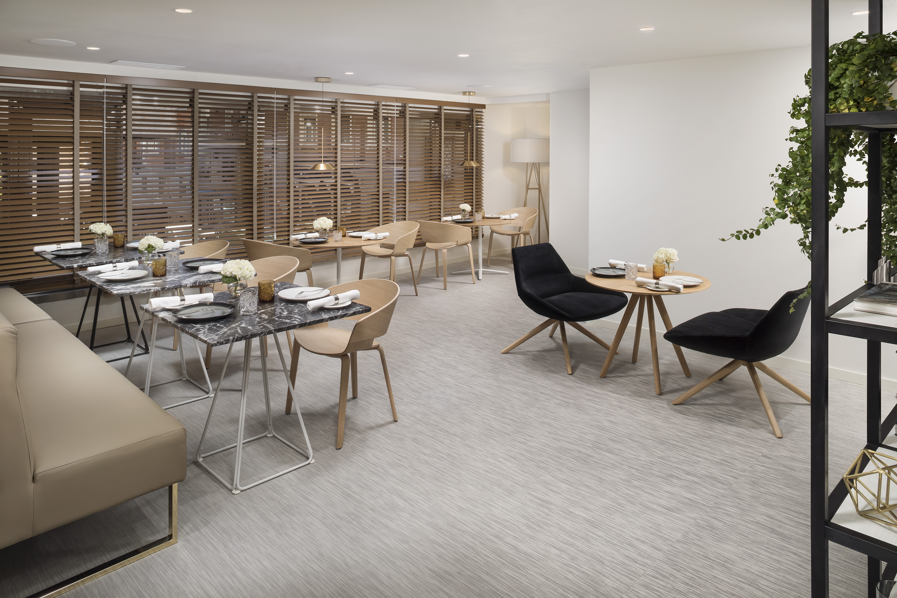 Contemporary restaurant interior with diverse seating, marble tables, and wood blinds.
