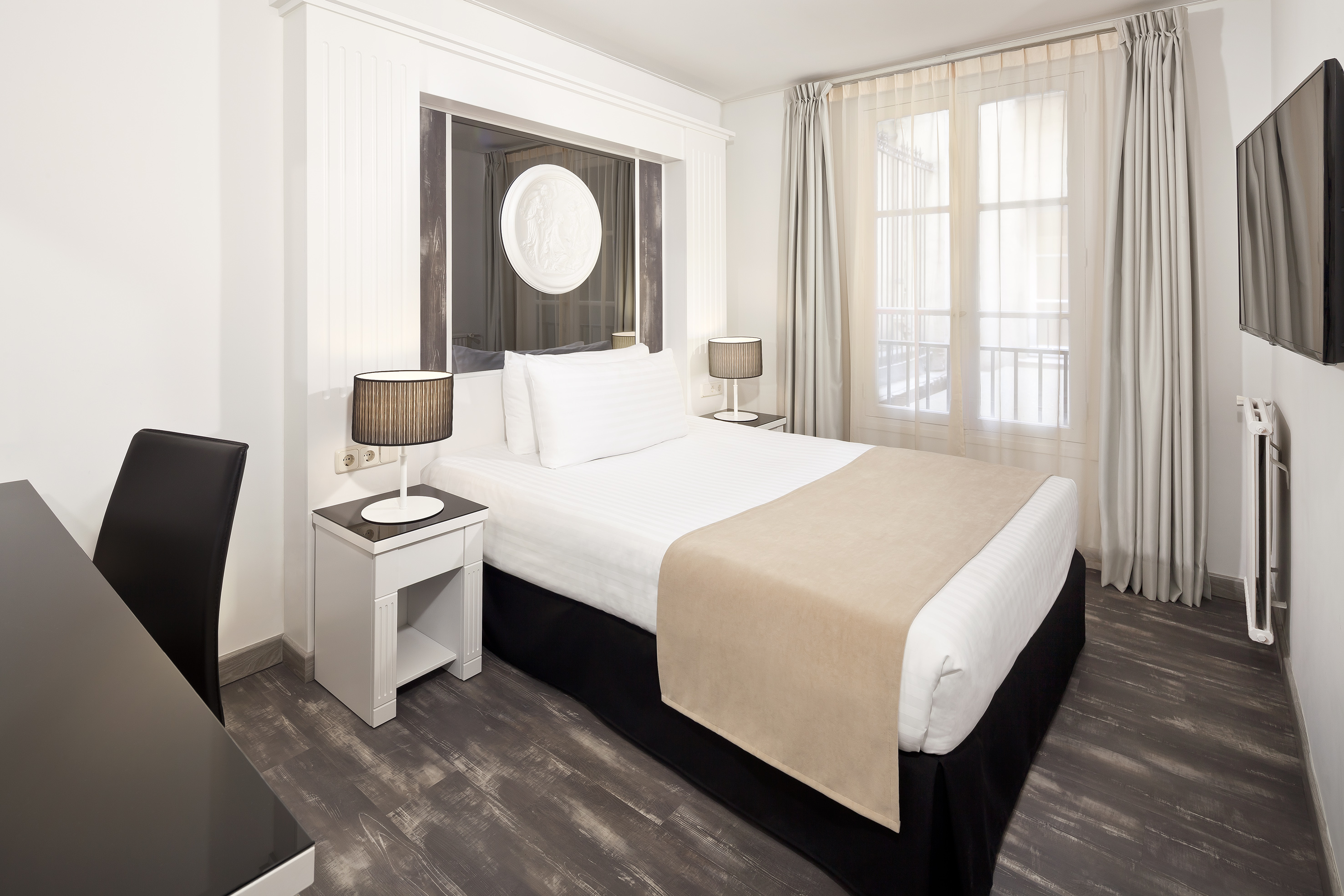 Modern hotel room with white bed, dark wood floor, window, and wall-mounted TV.