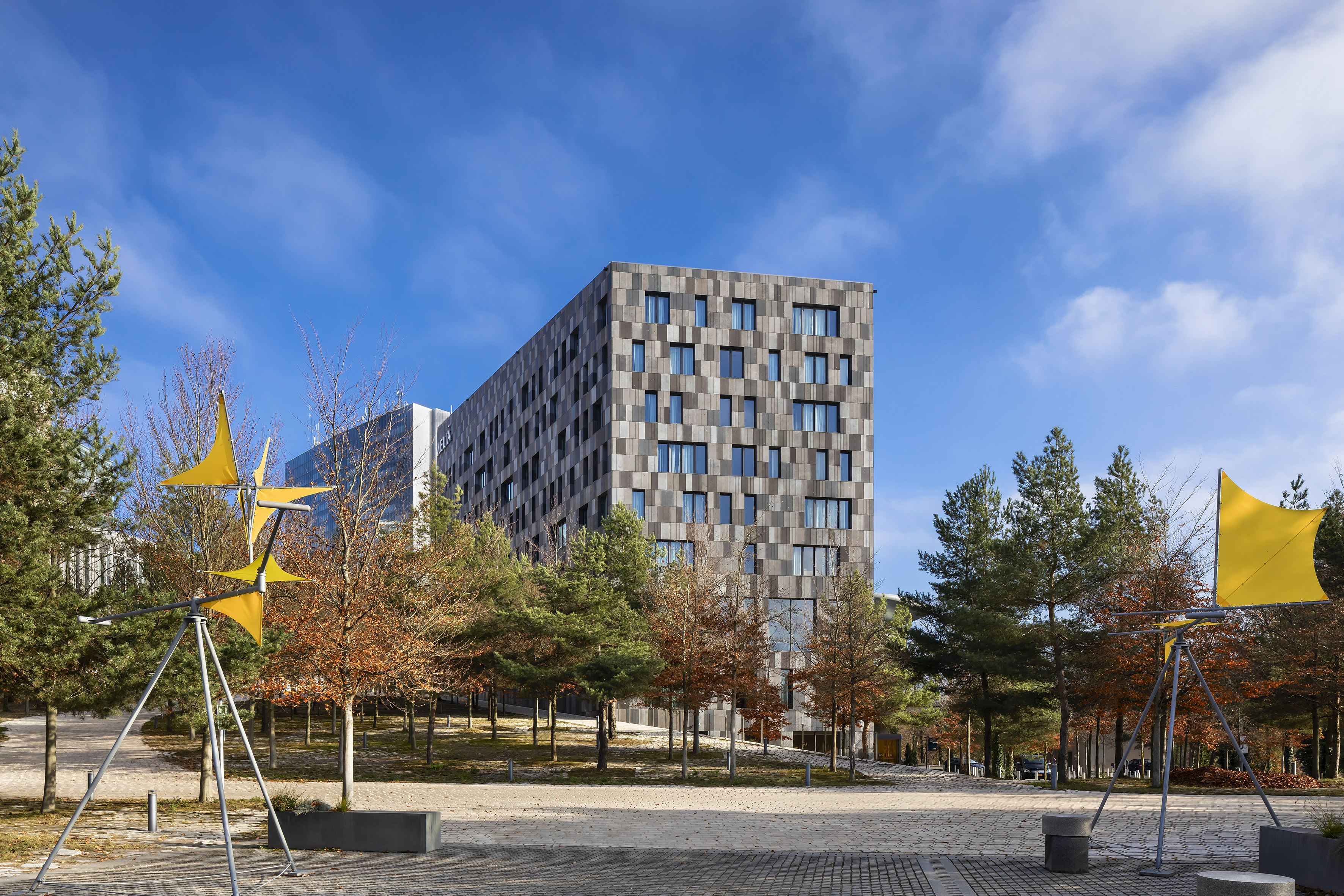 Melia building, patterned facade, urban park with trees and yellow wind art.