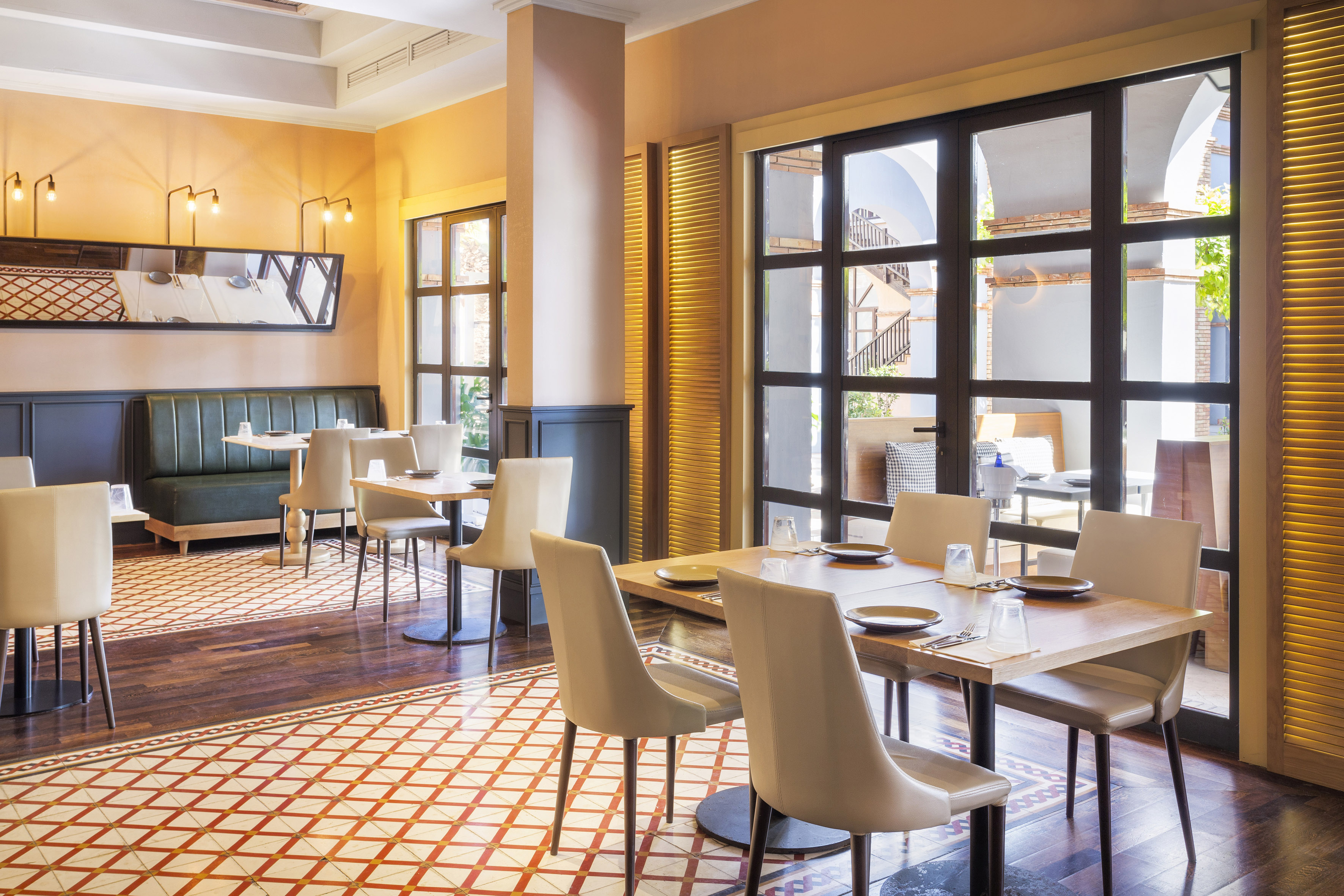 Modern restaurant dining room with patterned floor, booth seating, and large windows.
