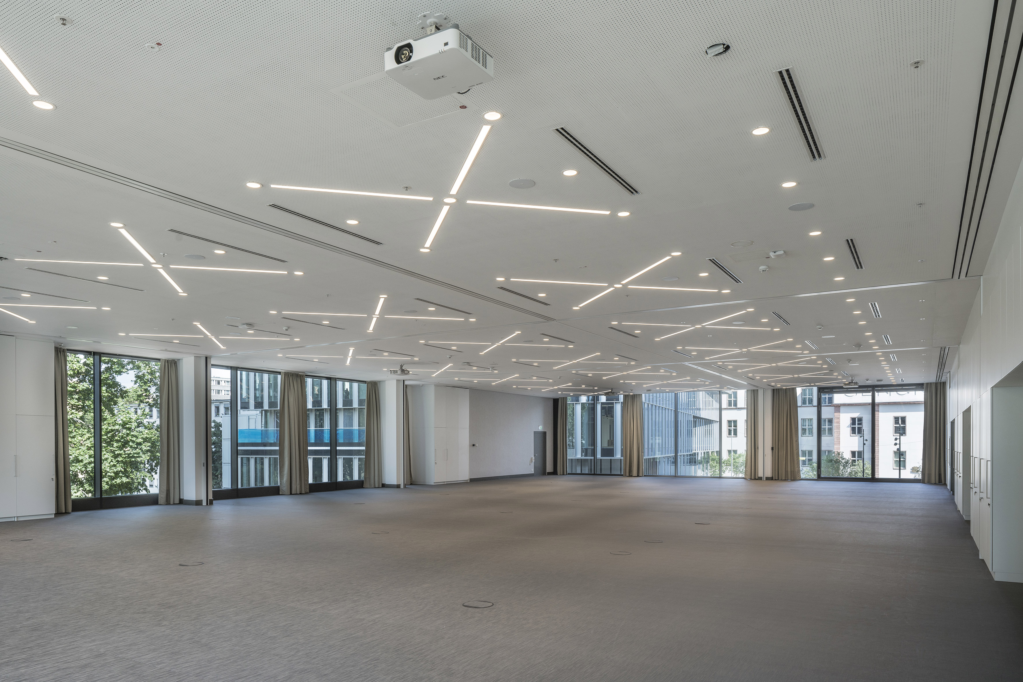 Empty modern event space with linear ceiling lights and projector.