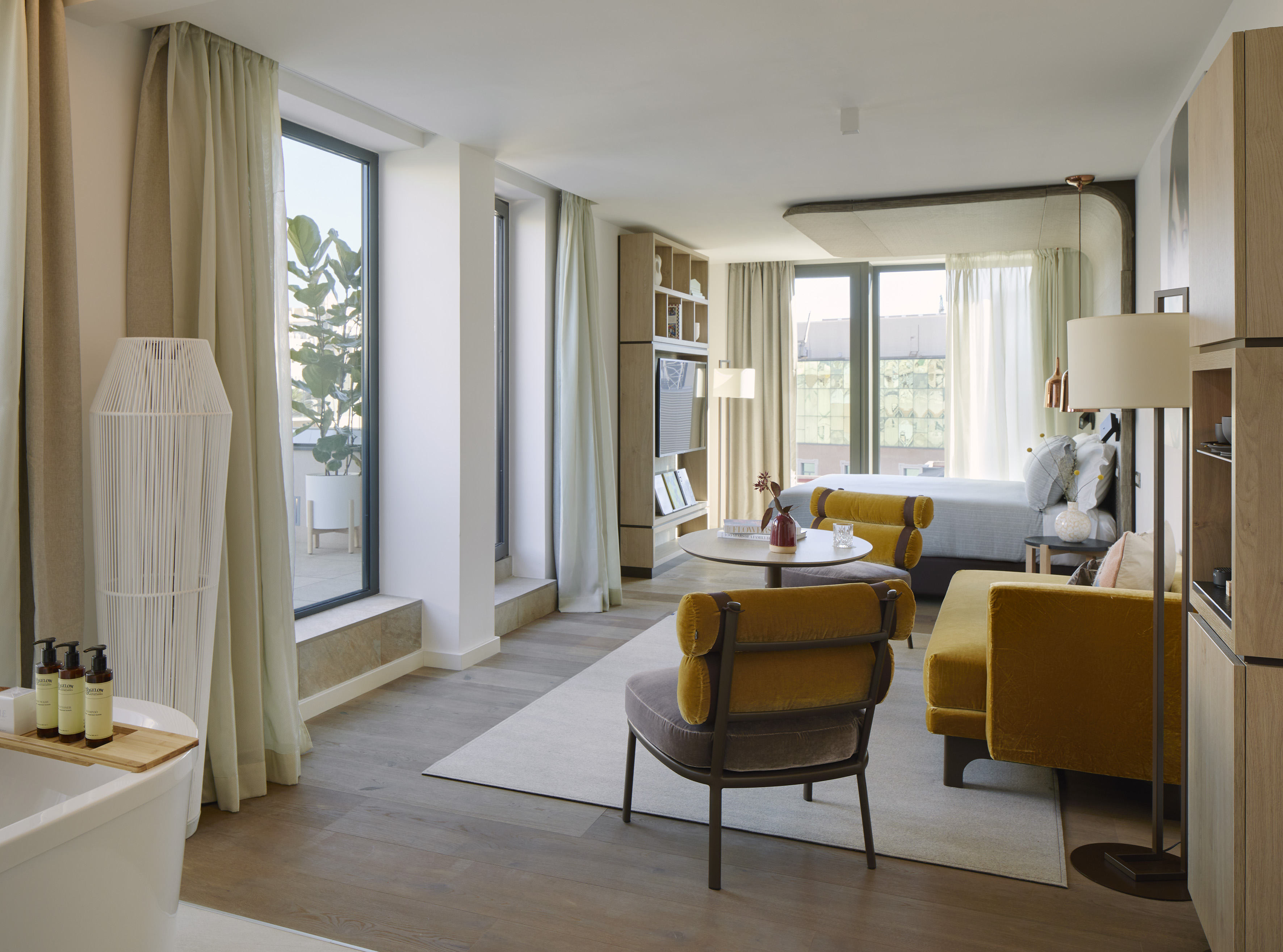 Modern hotel suite with living area, bedroom, bathtub, and large windows.