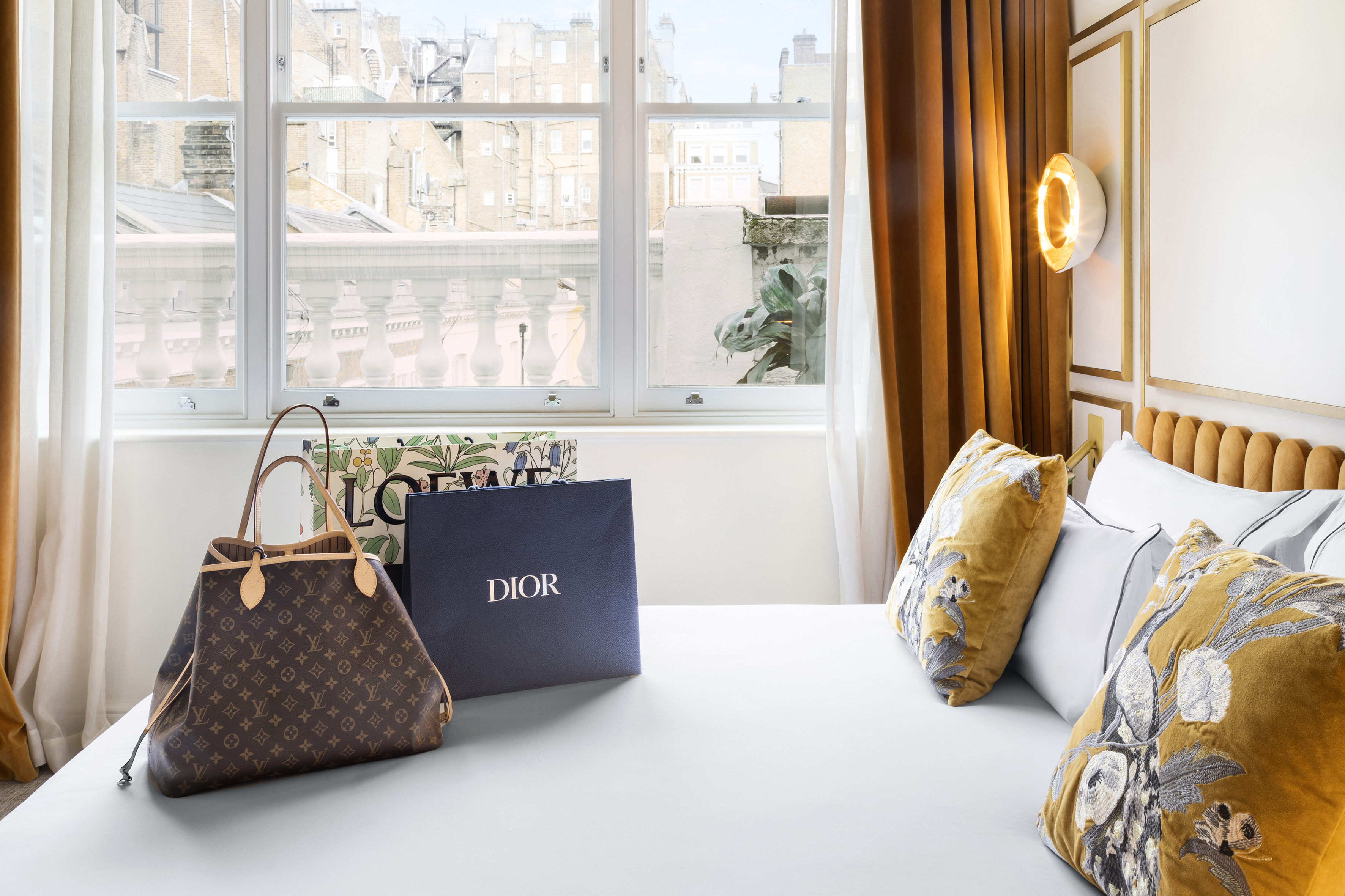Luxury Louis Vuitton bag and Dior shopping bag on bed in stylish hotel room.
