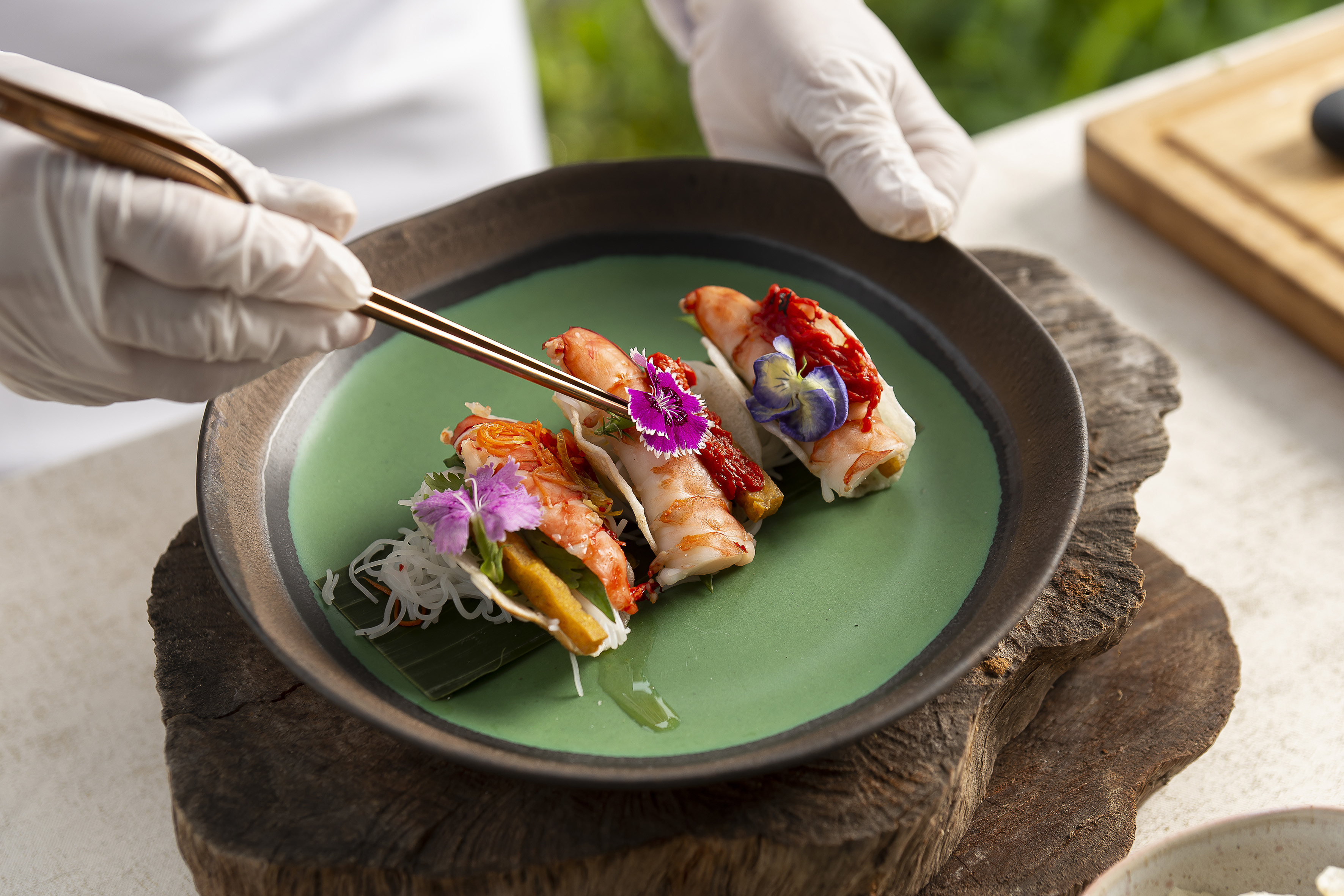 Chef garnishing gourmet shrimp spring rolls with colorful edible flowers.