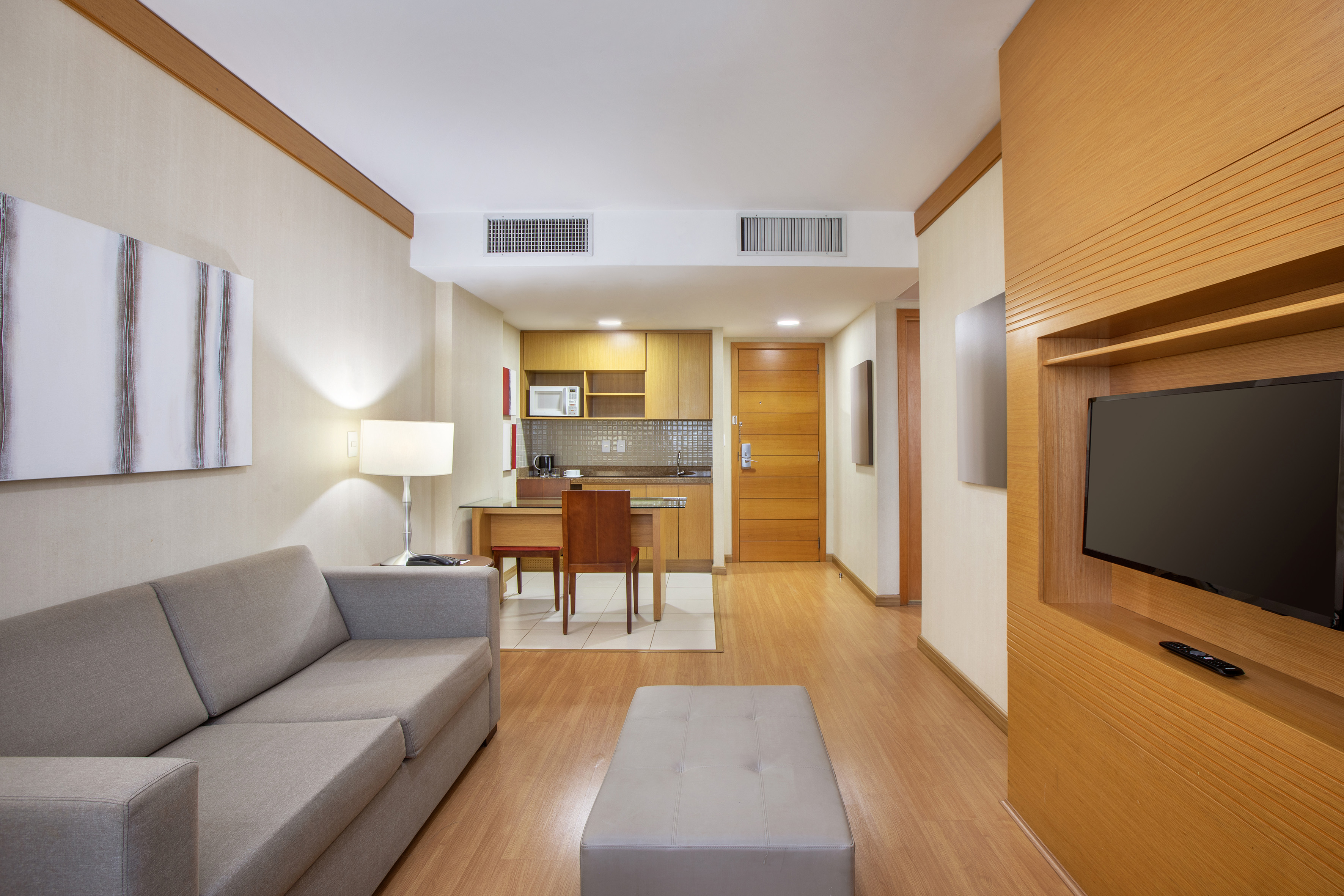 Modern hotel studio with living area, kitchenette, gray sofa, and TV.