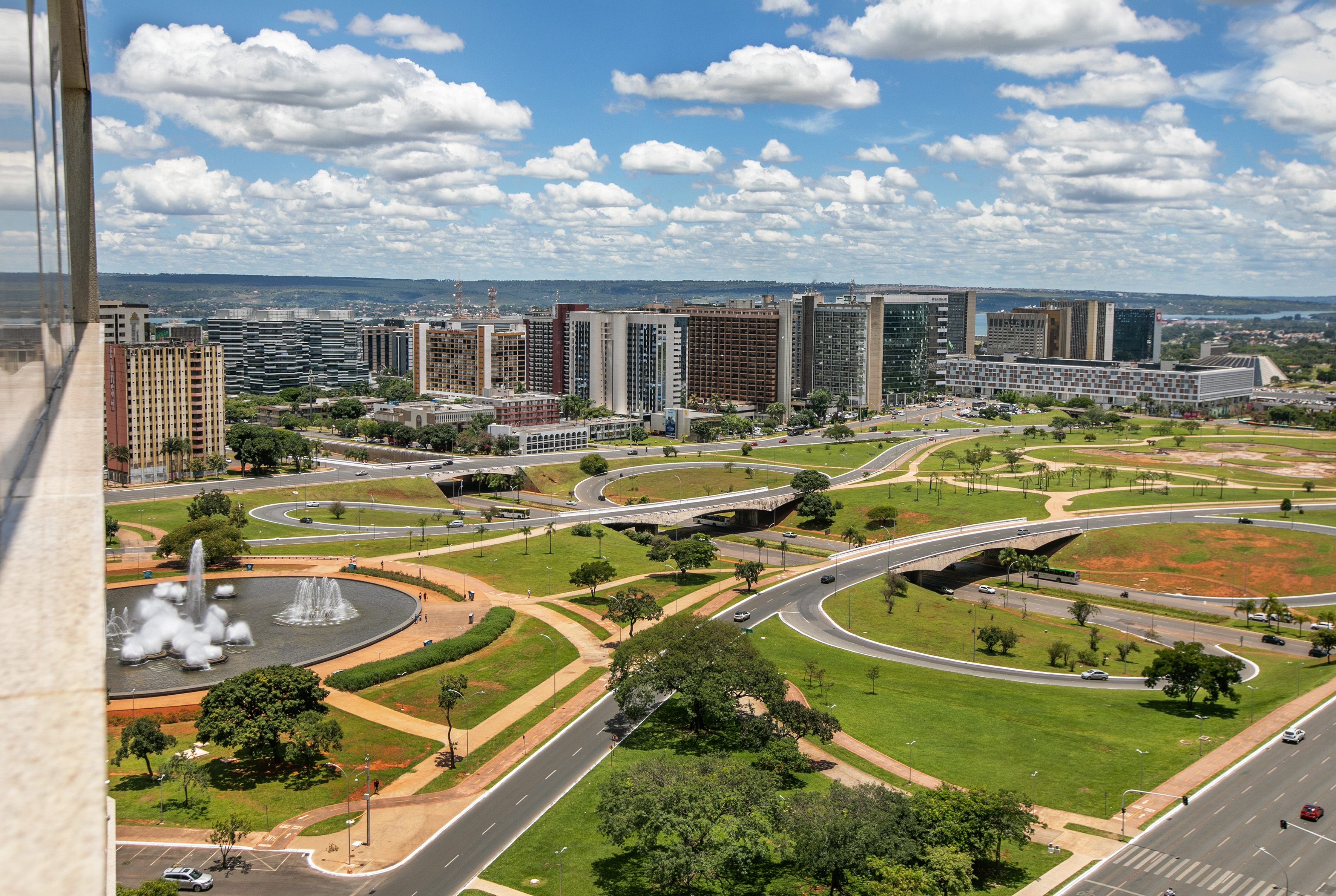 Brasilia city view: modern buildings, curved roads, green parks, large fountain.