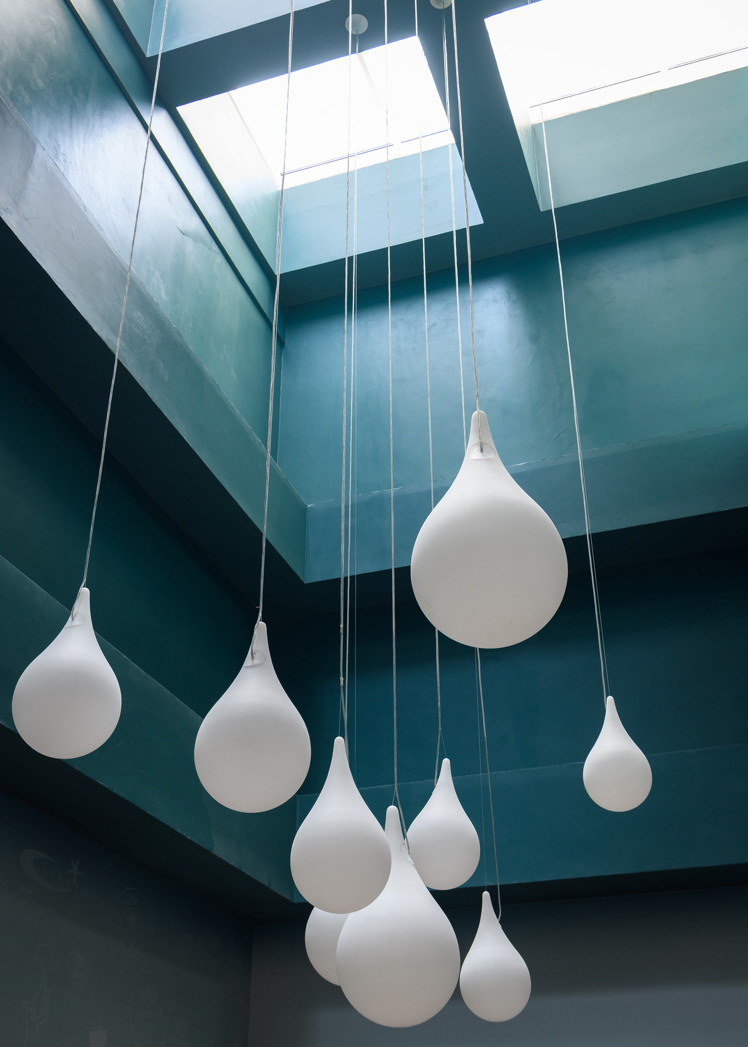 White teardrop pendant lights hanging from a teal ceiling with skylights.