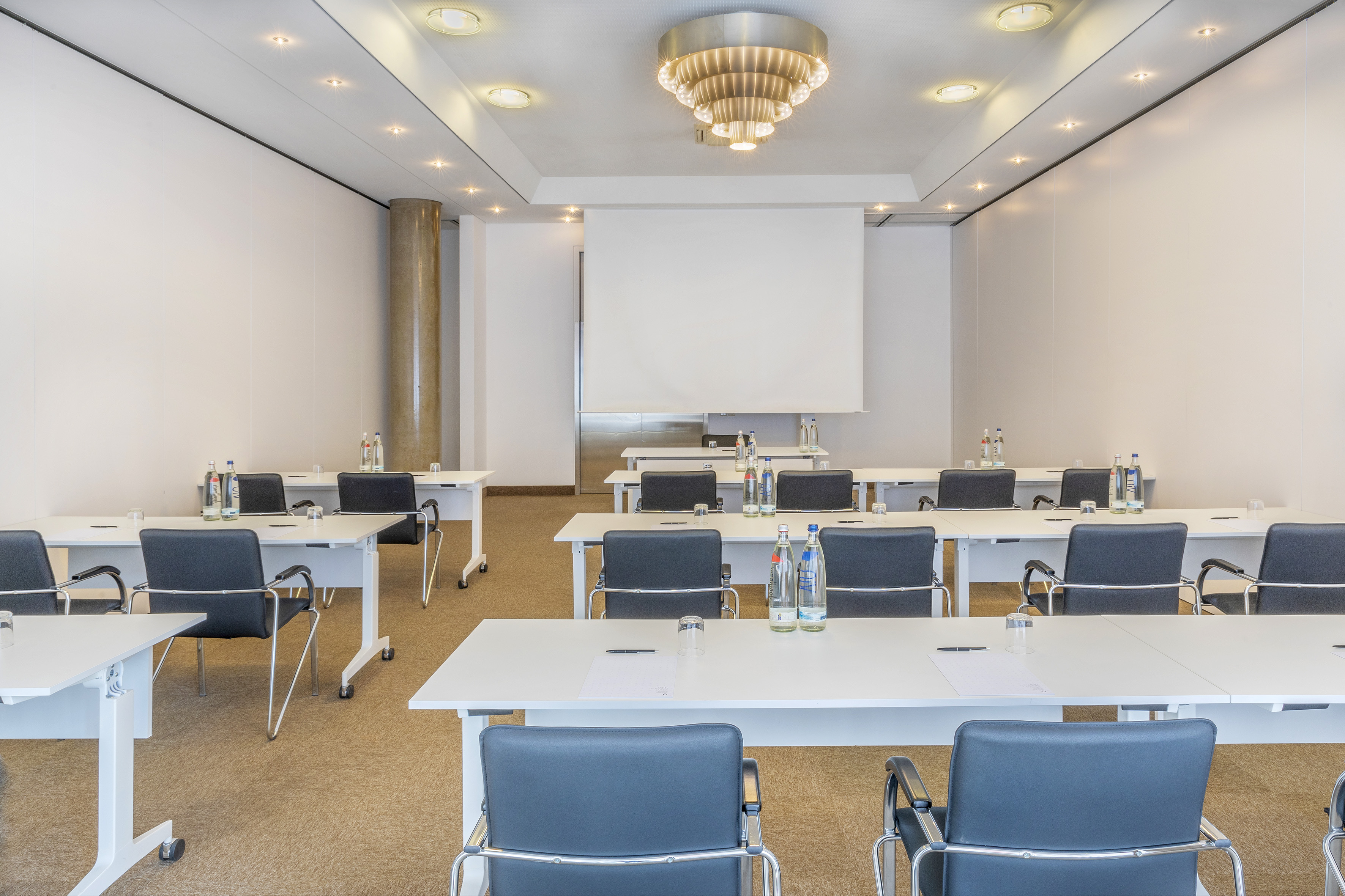 Bright conference room with white tables, black chairs, and projector screen.