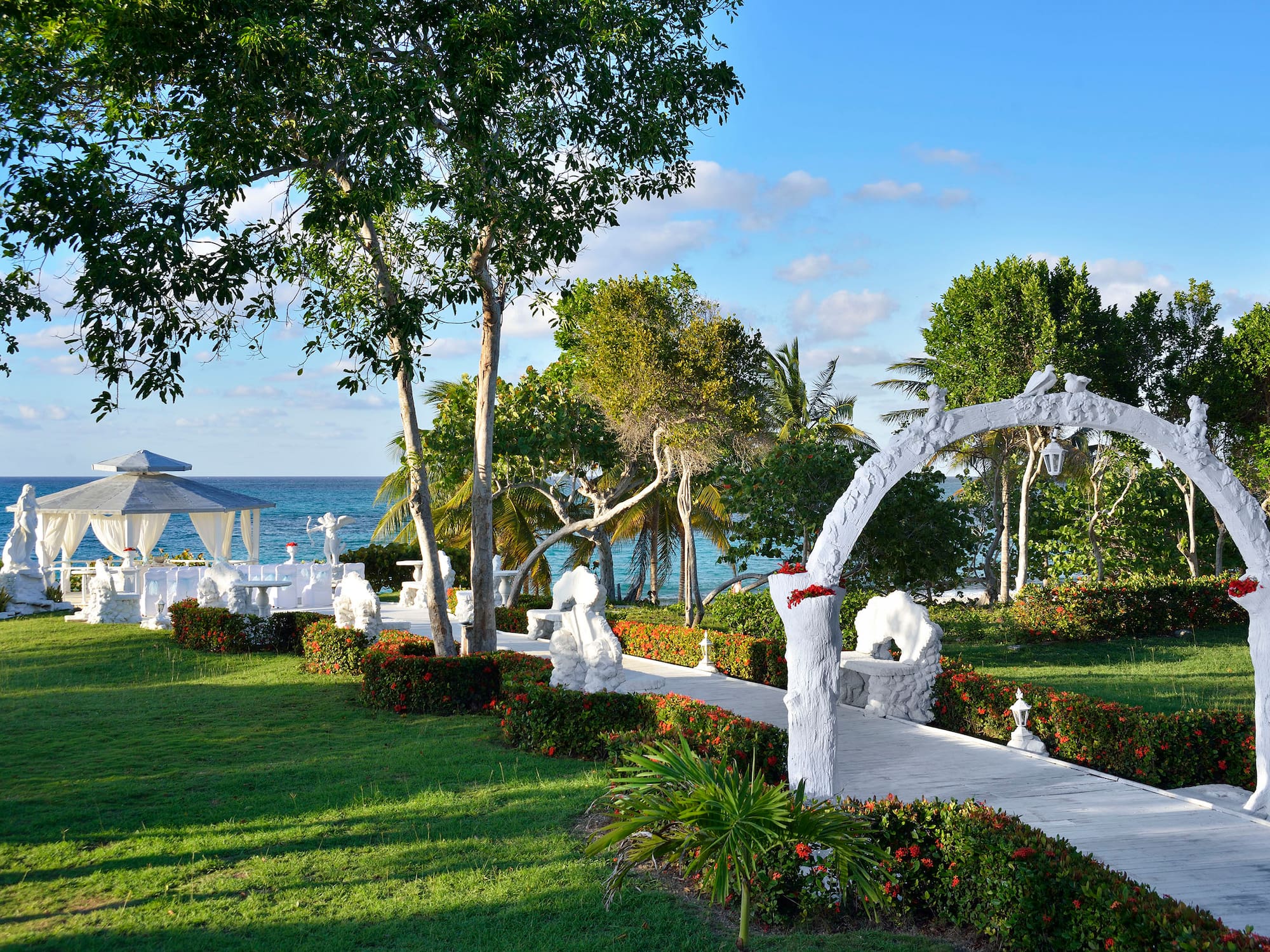 a white walkway with a white structure and trees and a beach