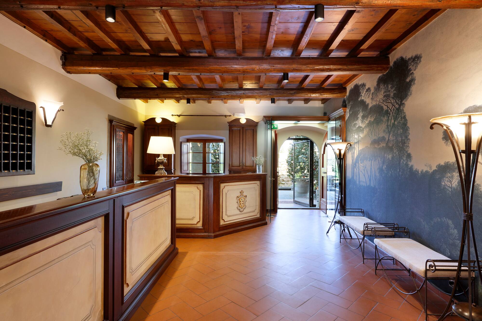 Hotel lobby with wooden beams, terracotta floor, reception, and tree mural.