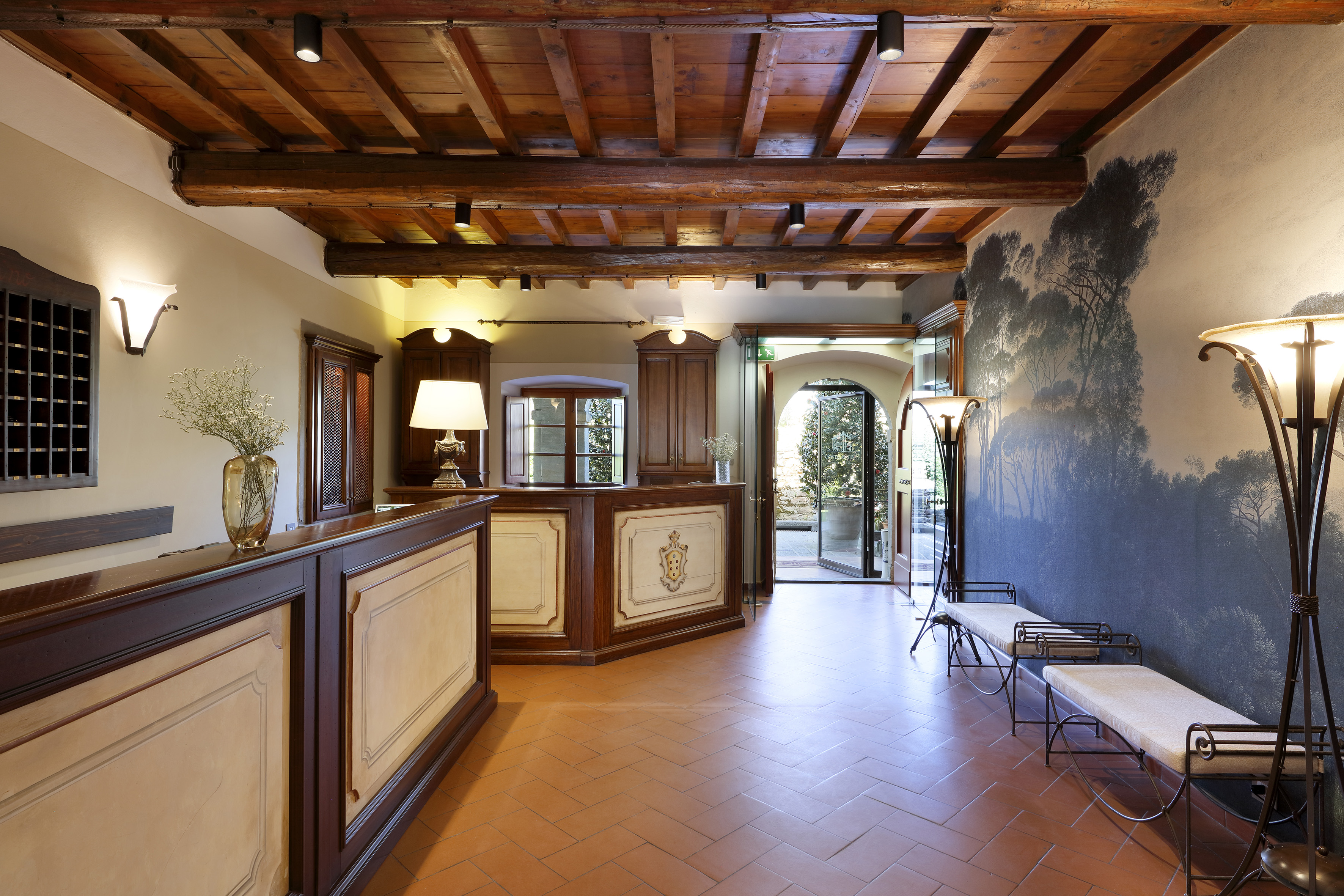 Hotel lobby with wooden beams, terracotta floor, reception, and tree mural.