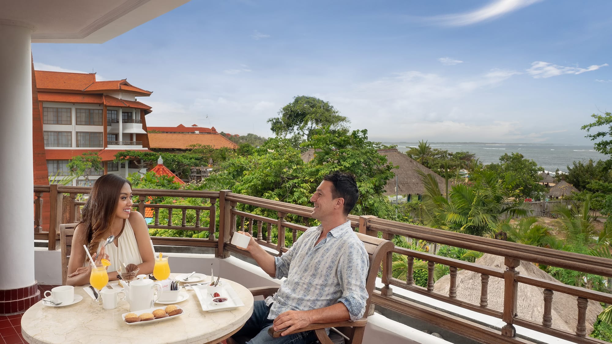 a man and woman sitting at a table with food on a balcony