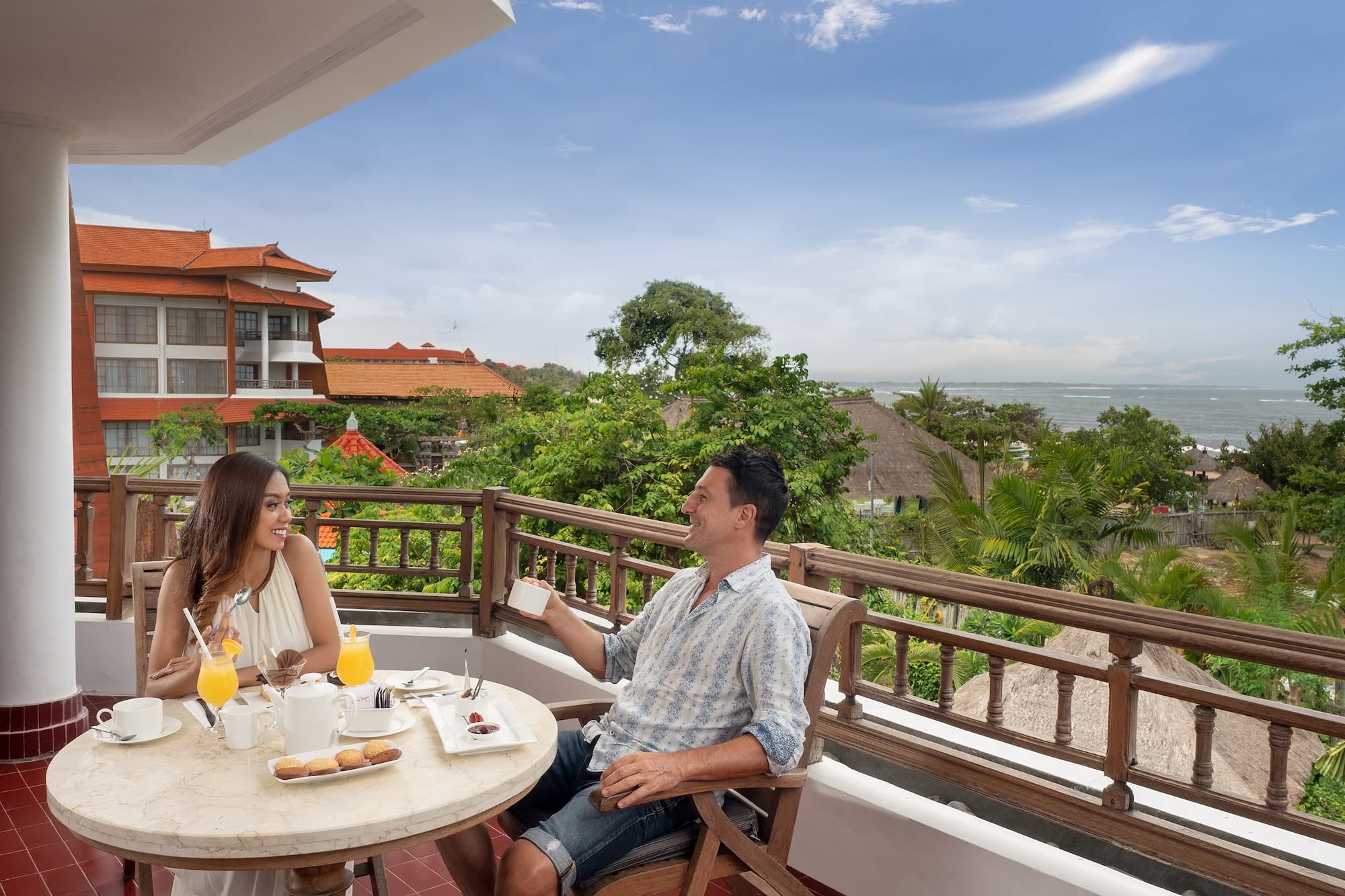 a man and woman sitting at a table with food on a balcony