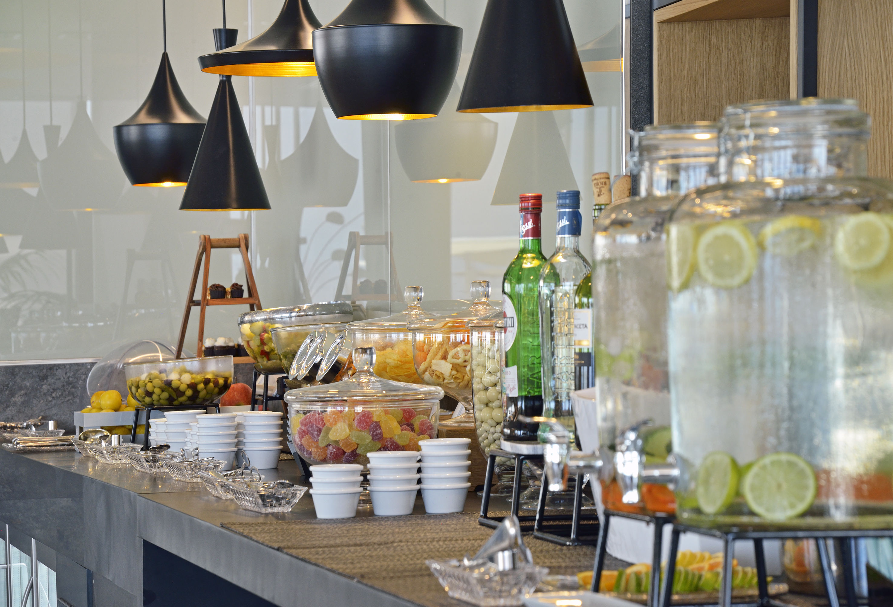 Hotel buffet display with snacks, fruit water, olives, and modern lighting.
