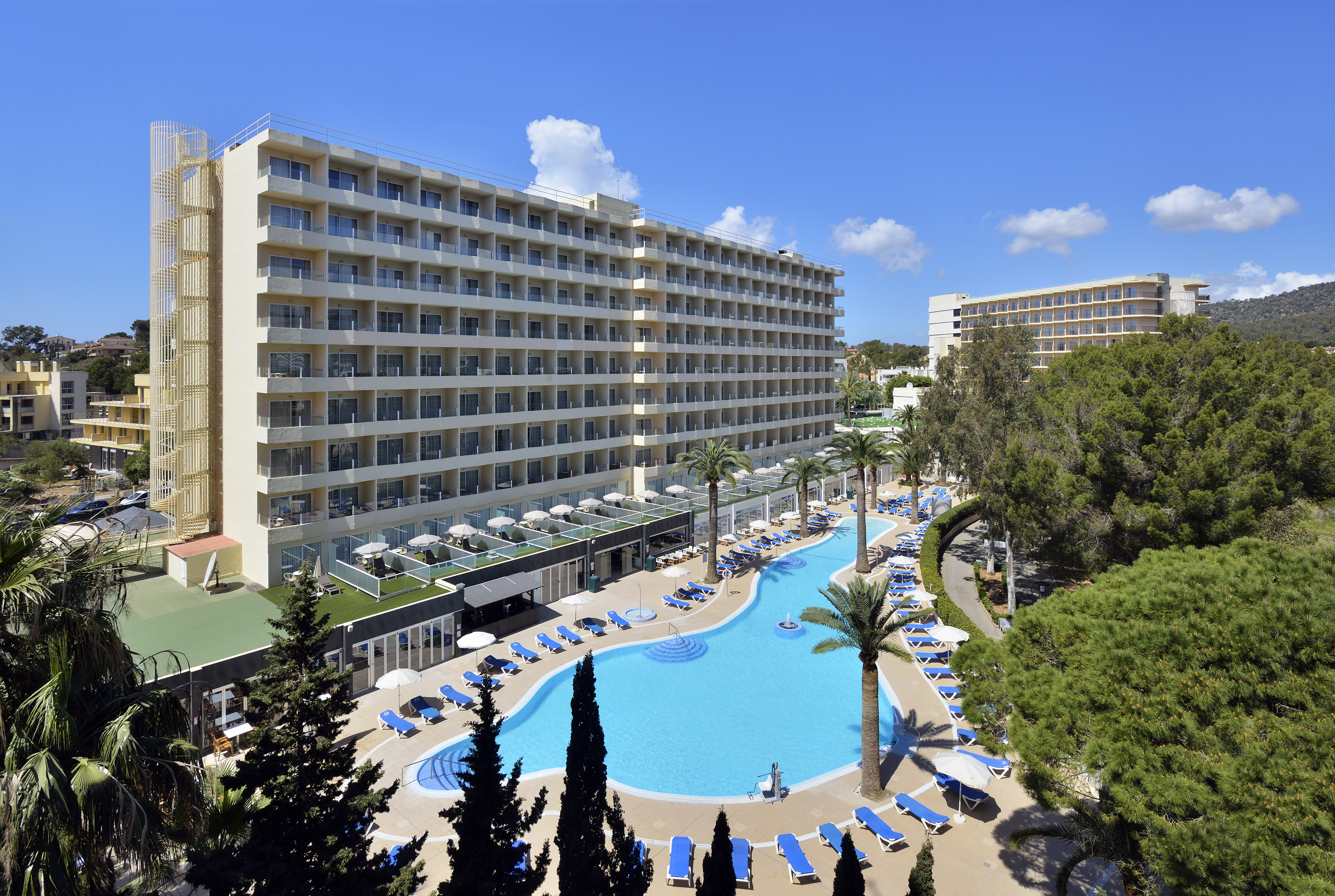 Sunny resort hotel with large outdoor pool, palm trees, and balconies.