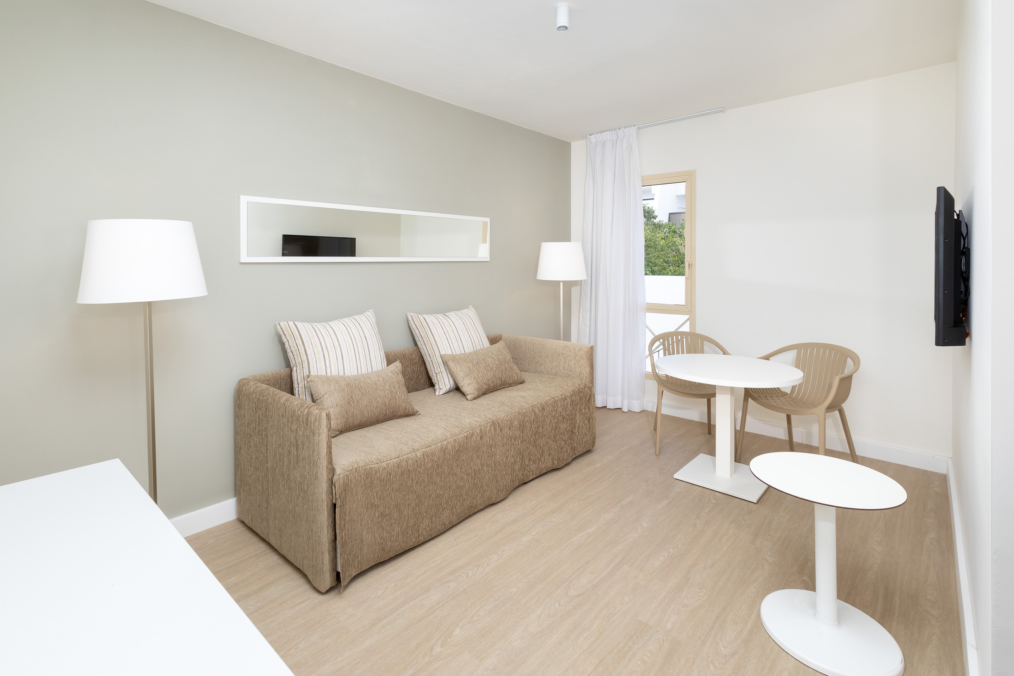 Modern studio apartment living area with sofa bed, dining table, and neutral decor.