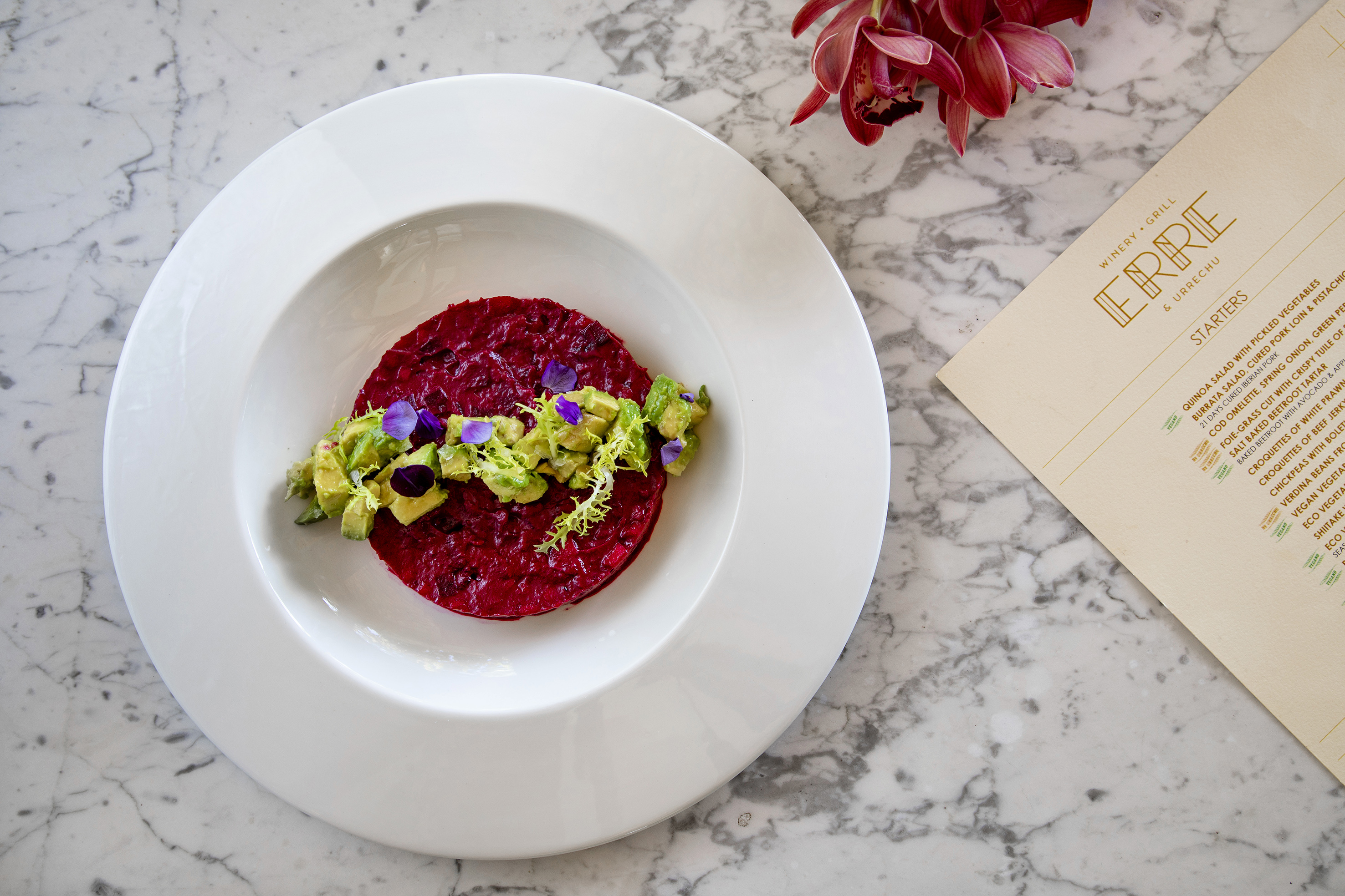 Beetroot tartare with avocado, edible flowers on white plate, restaurant menu.