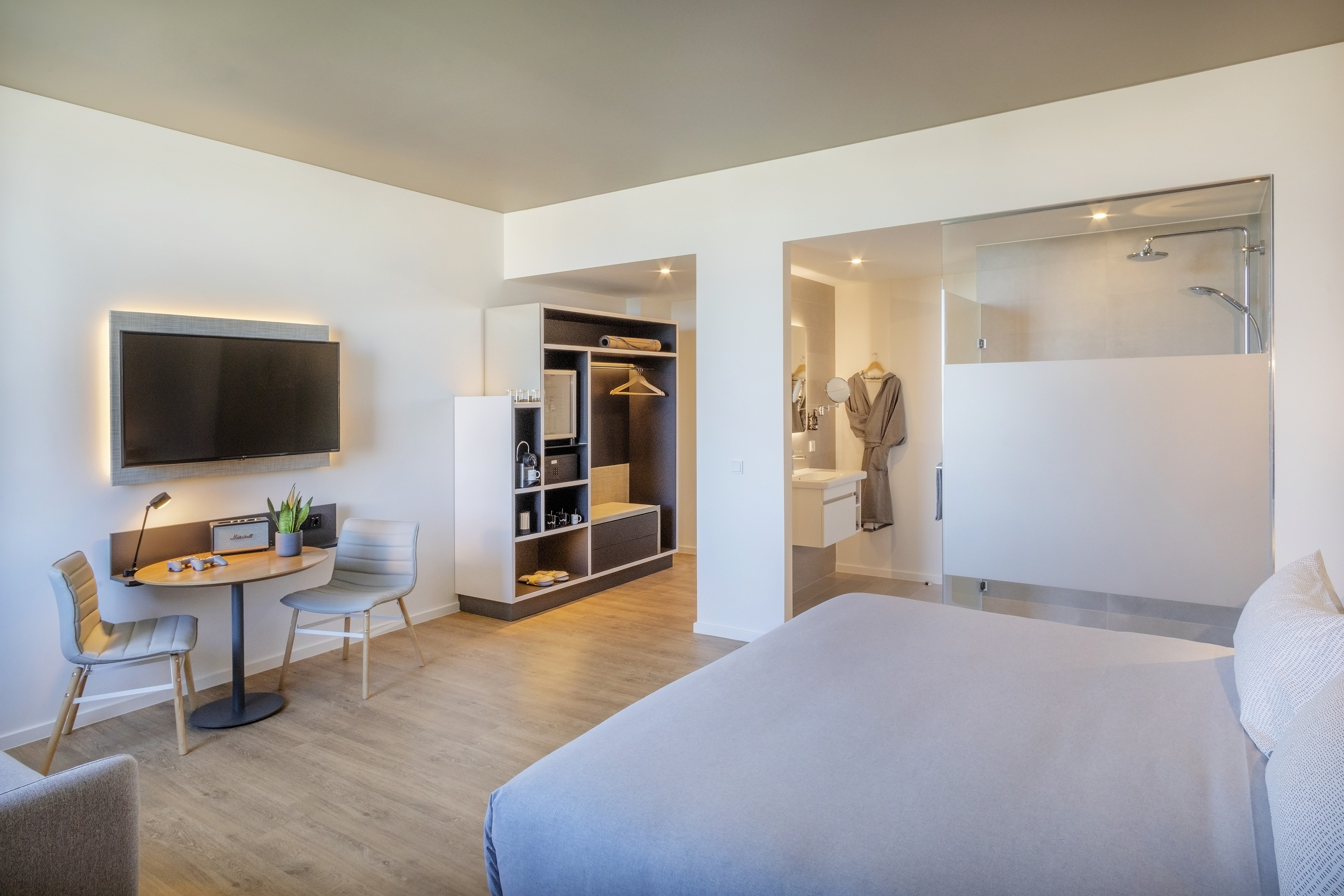 Modern hotel room with bed, TV, workspace, and glass-partitioned bathroom.