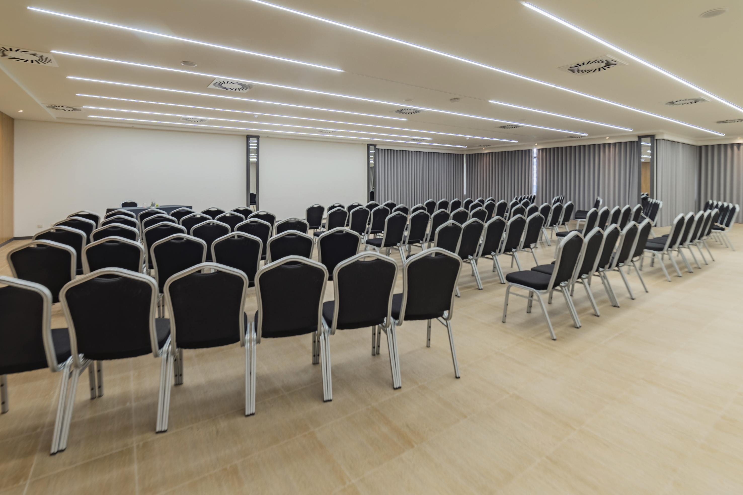 Empty modern conference room with rows of black chairs and linear ceiling lights.