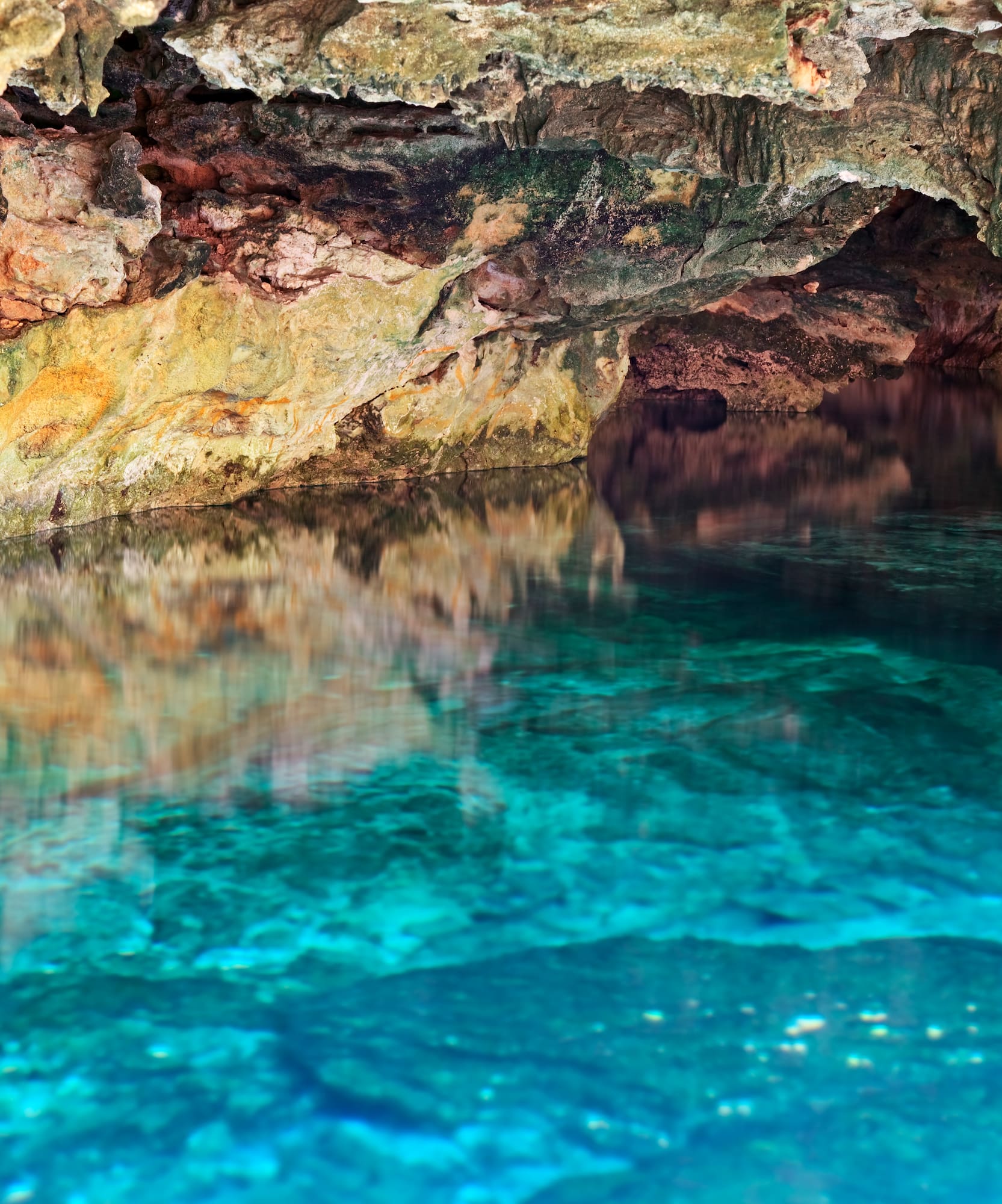 Turquoise water reflects rocky cave walls in a natural cenote.