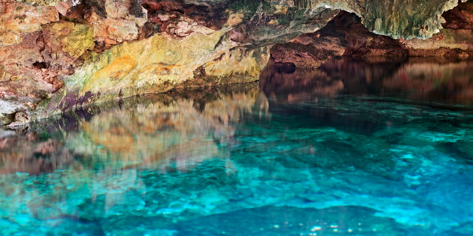 Cenote interior with vibrant turquoise water reflecting colorful rock formations.