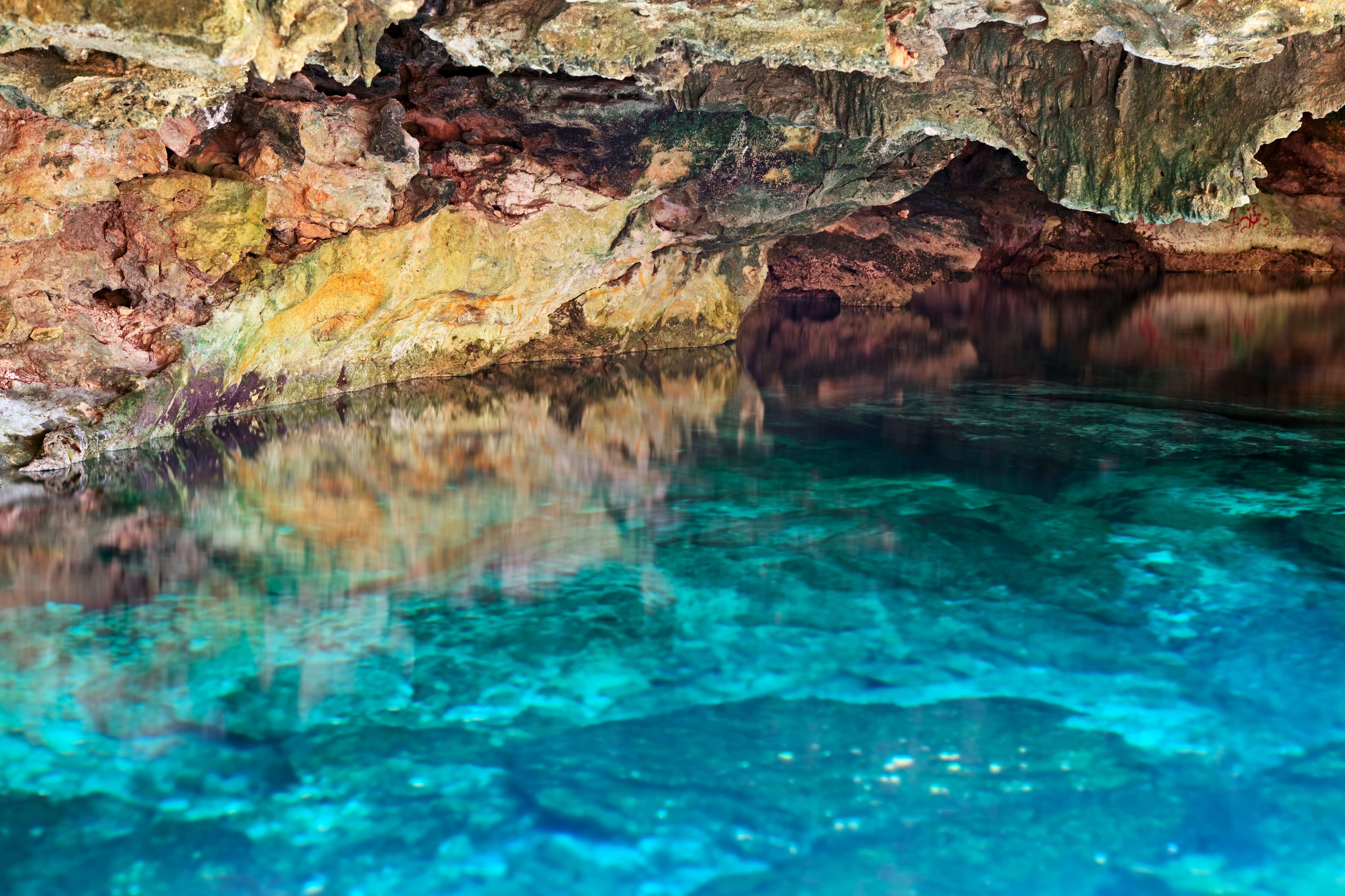 Turquoise water reflects rocky cave walls in a natural cenote.