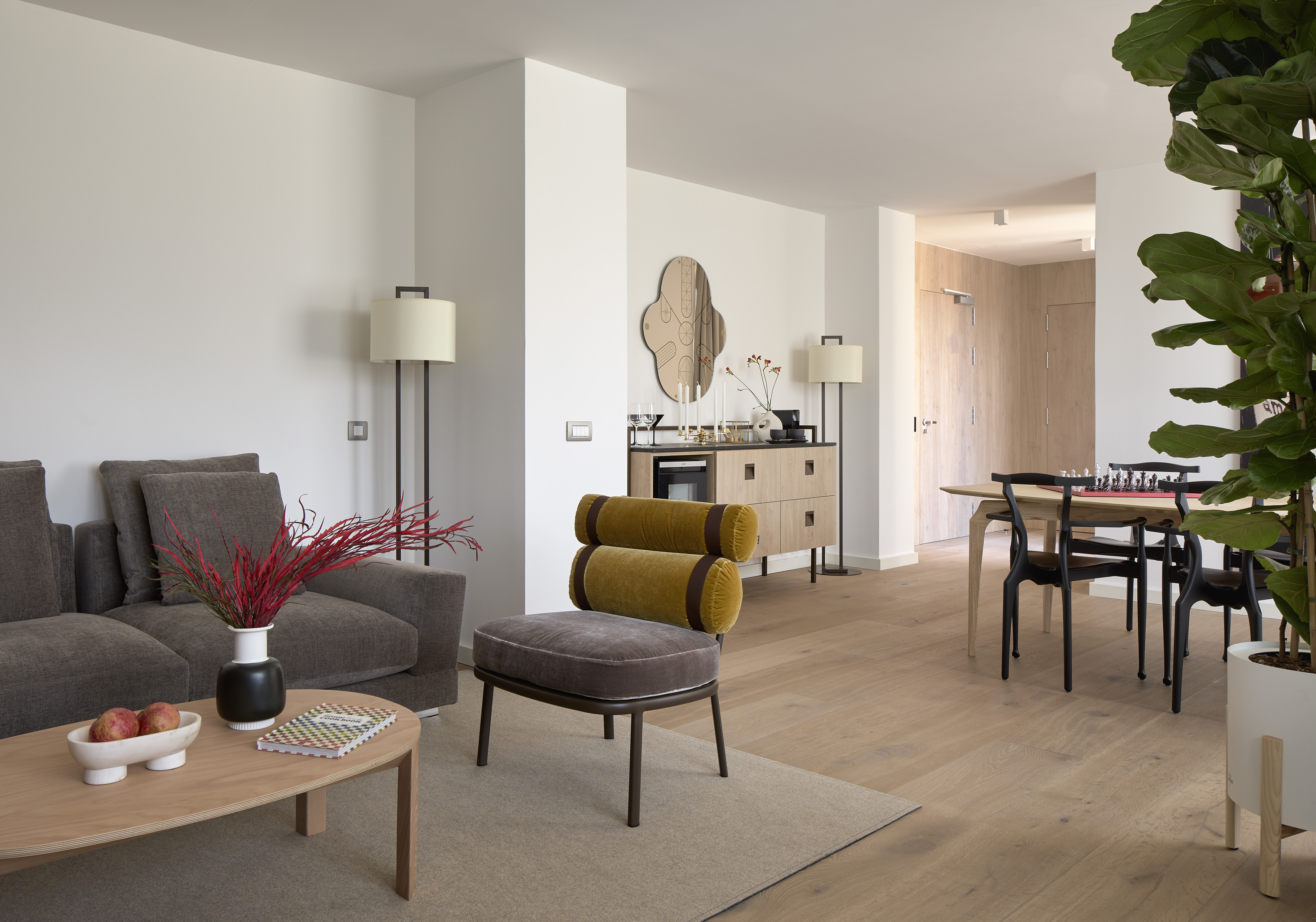 Modern living room with grey sofa, yellow armchair, dining table, wood floor.