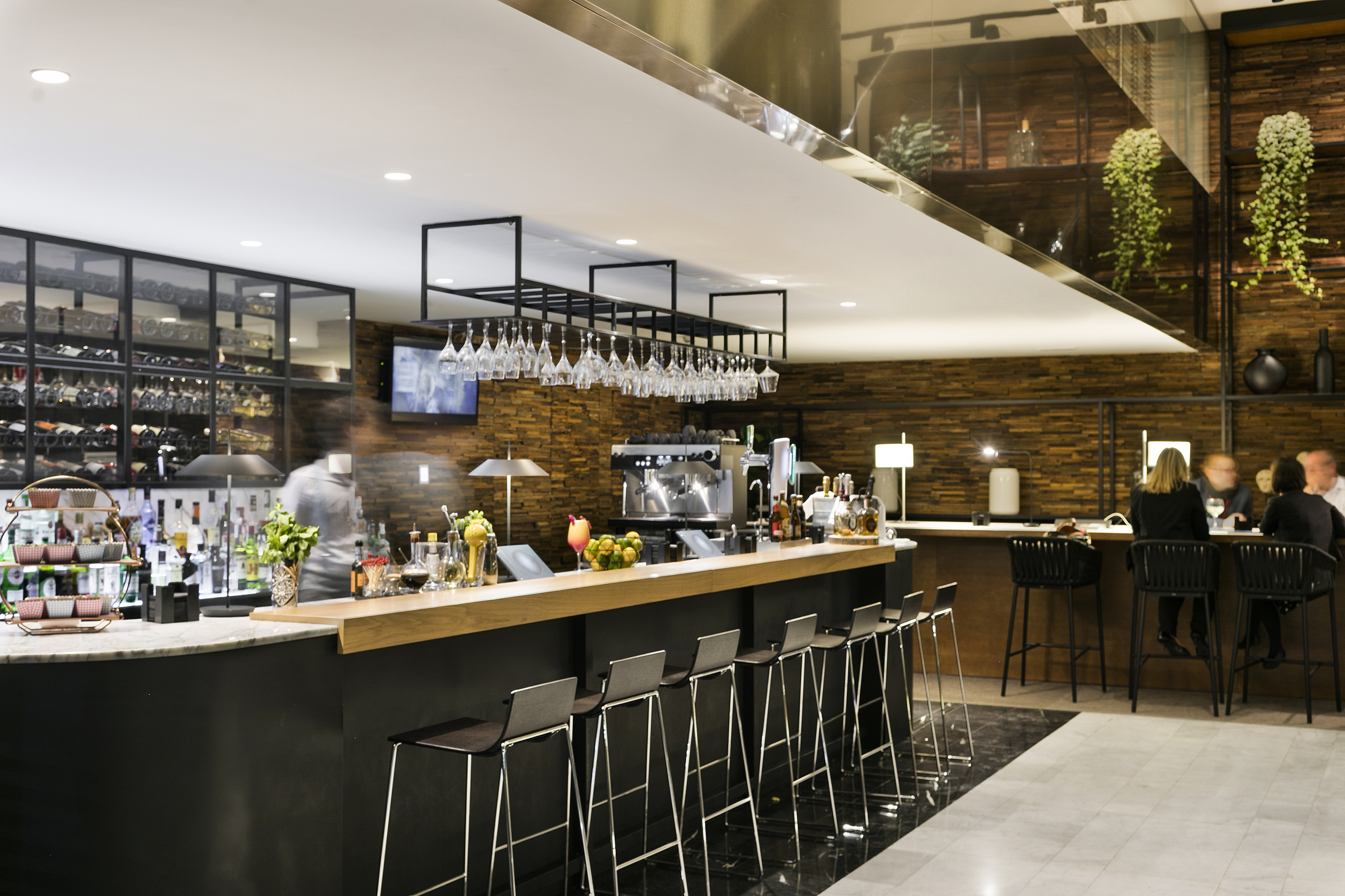 Modern bar interior with long counter, bar stools, wine, and blurred bartender.