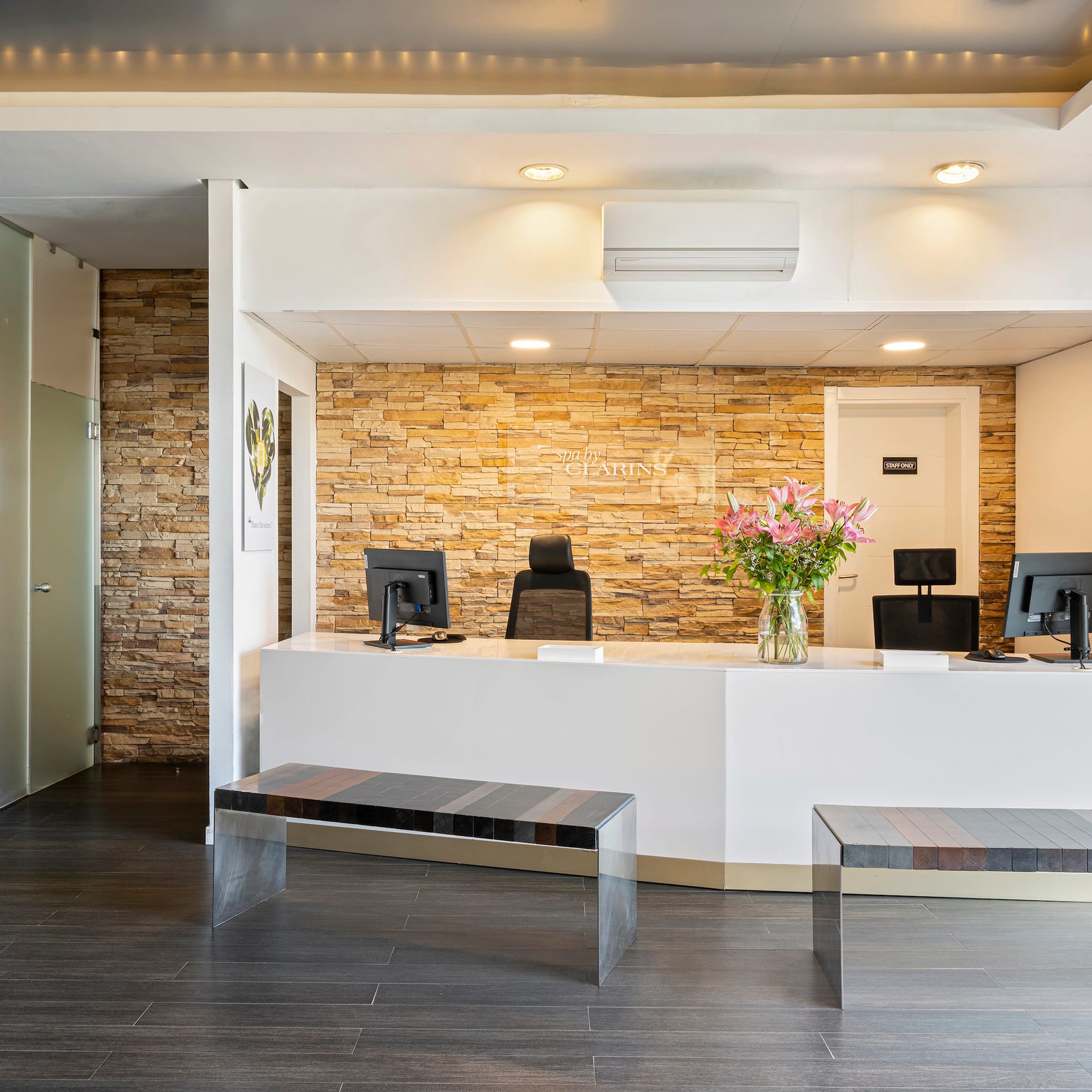 Modern Clarins spa reception with white desk and stone accent wall.