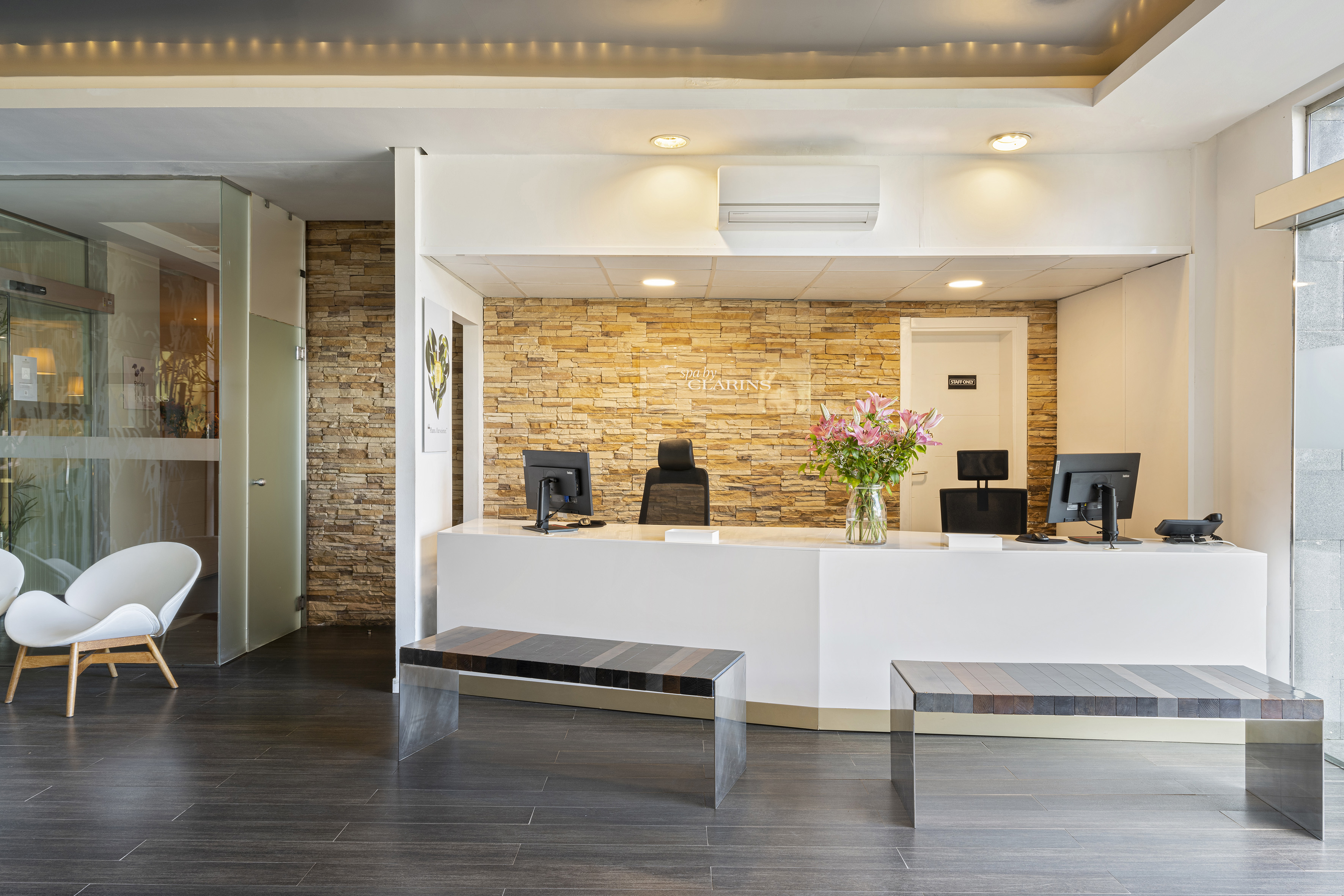 Clarins spa reception with modern white desk, stone wall, and contemporary lounge.