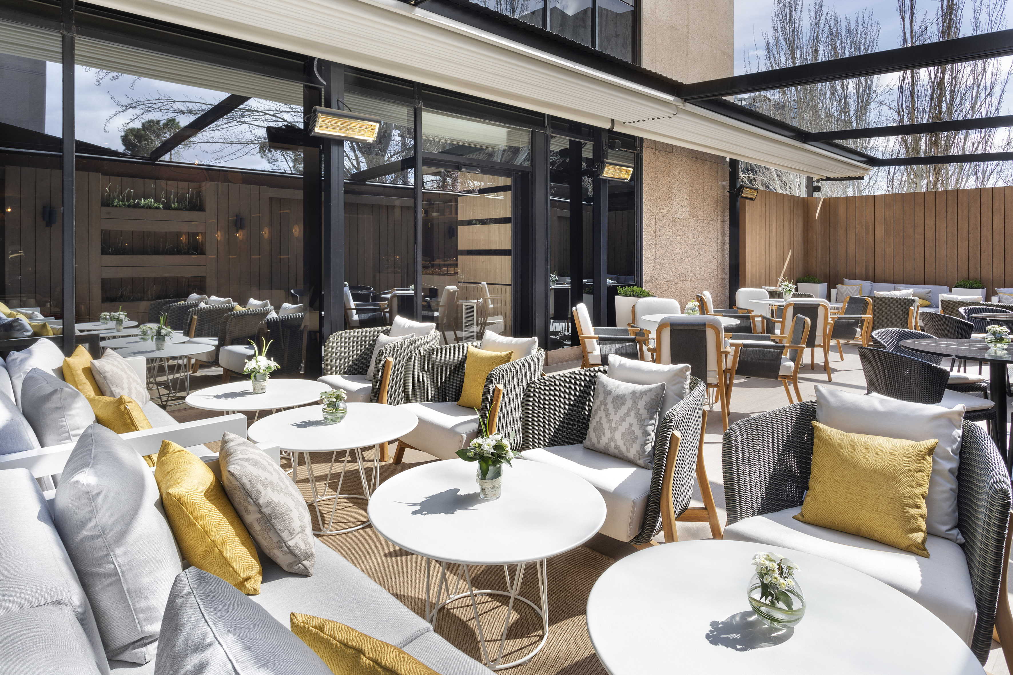 Modern outdoor patio with grey and yellow seating, white tables, and heaters.