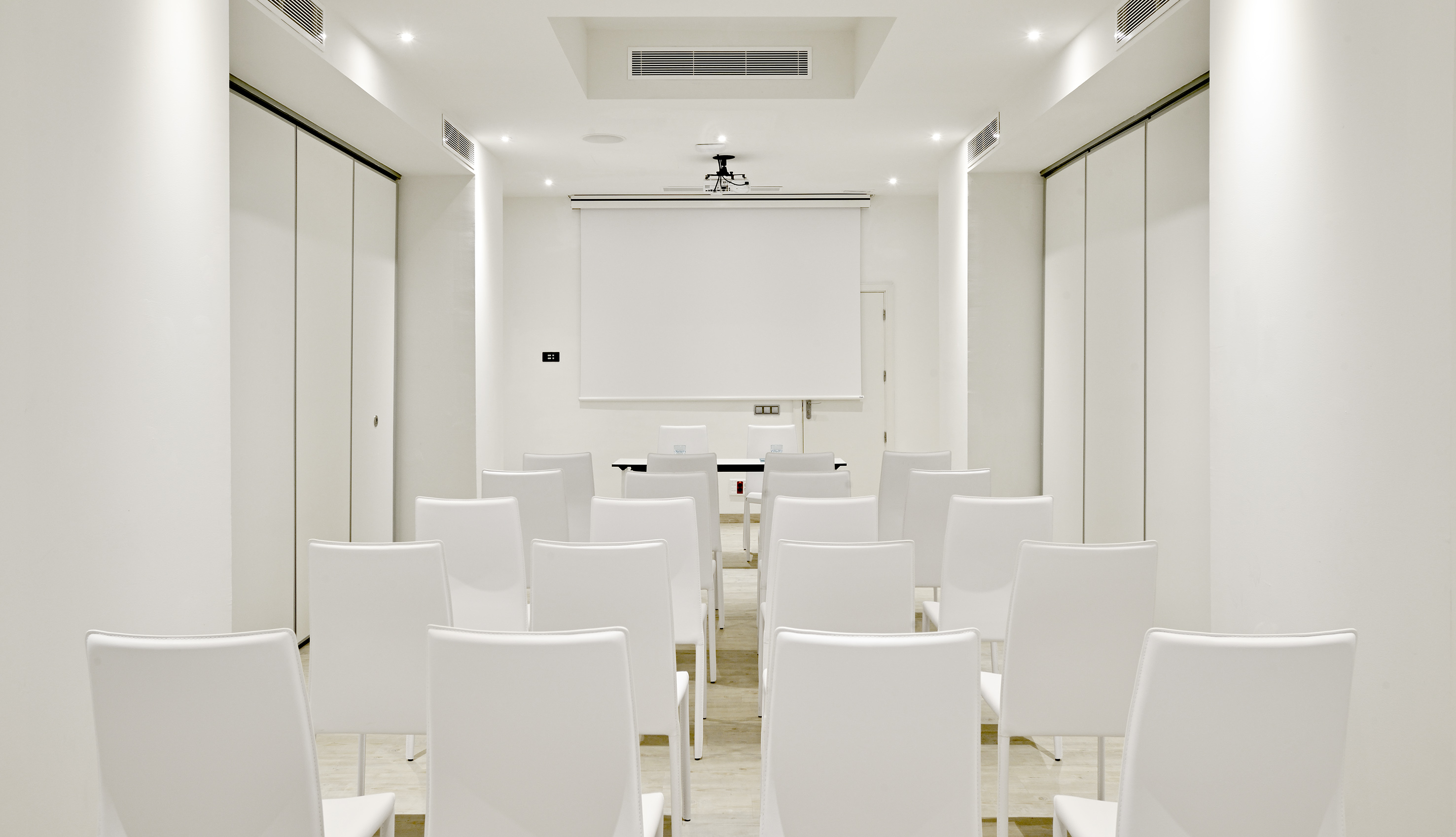 Modern conference room setup: white chairs, projector screen, minimalist design.