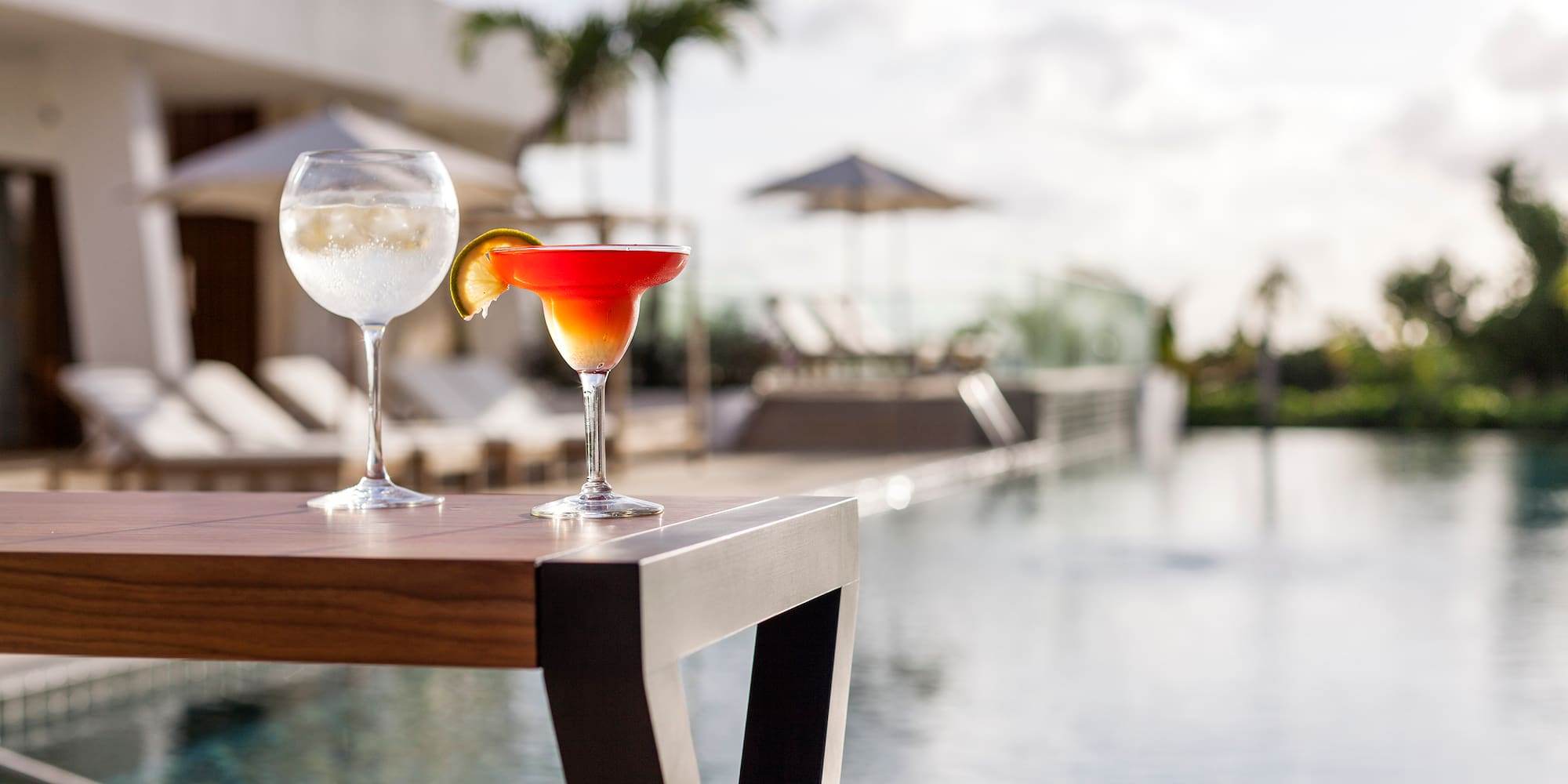 two glasses of drinks on a table by a pool