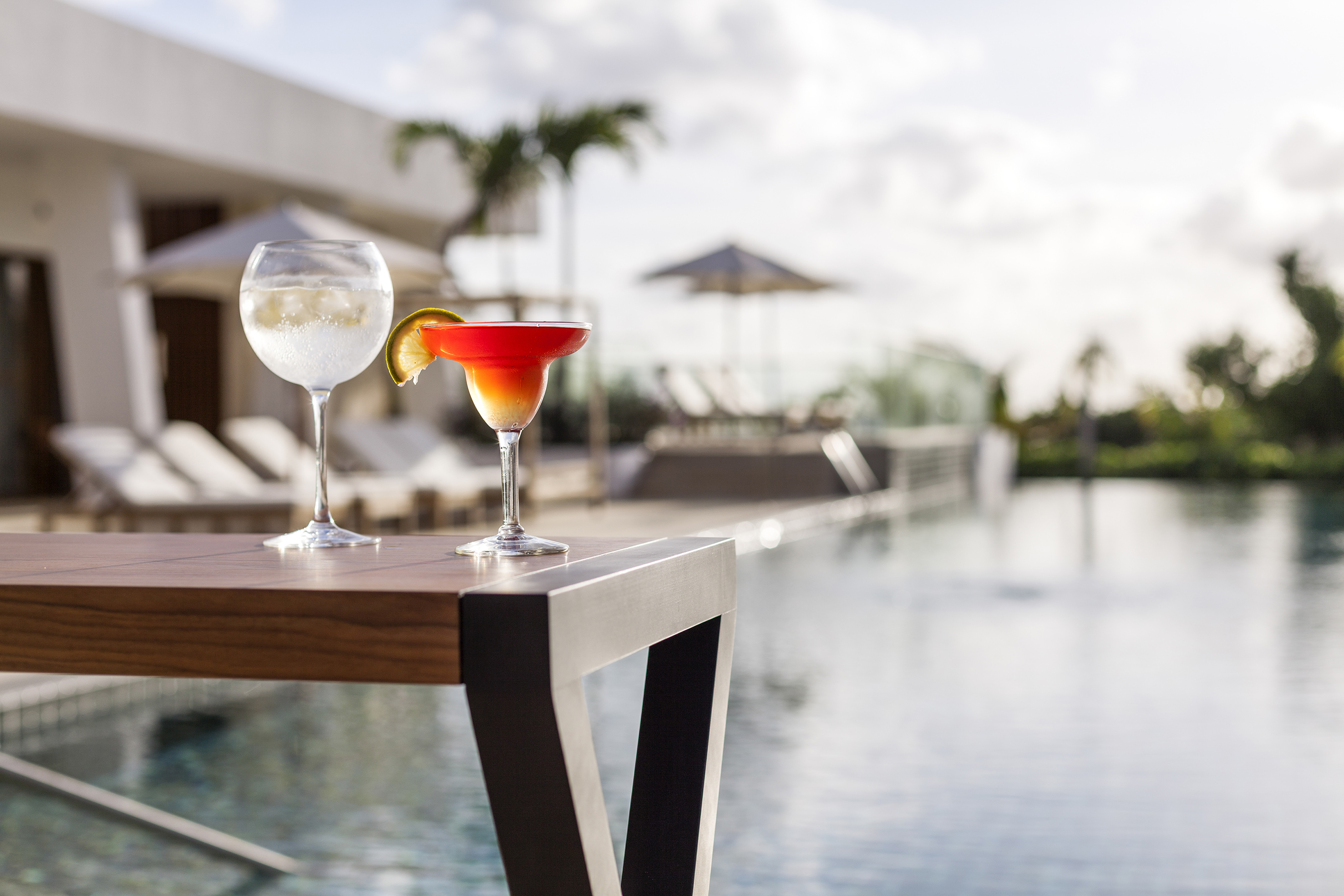 two glasses of drinks on a table by a pool