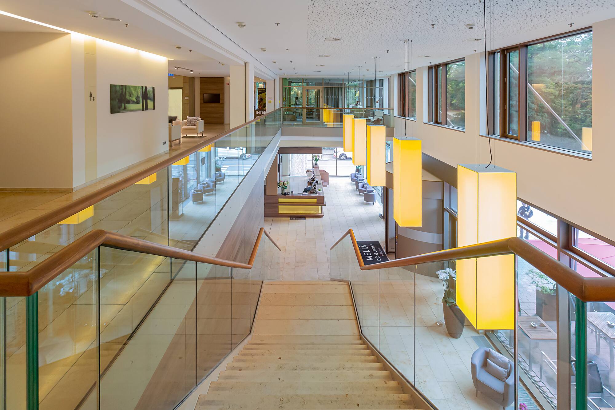 Modern hotel lobby with grand staircase, glass railing, and brightly lit reception.