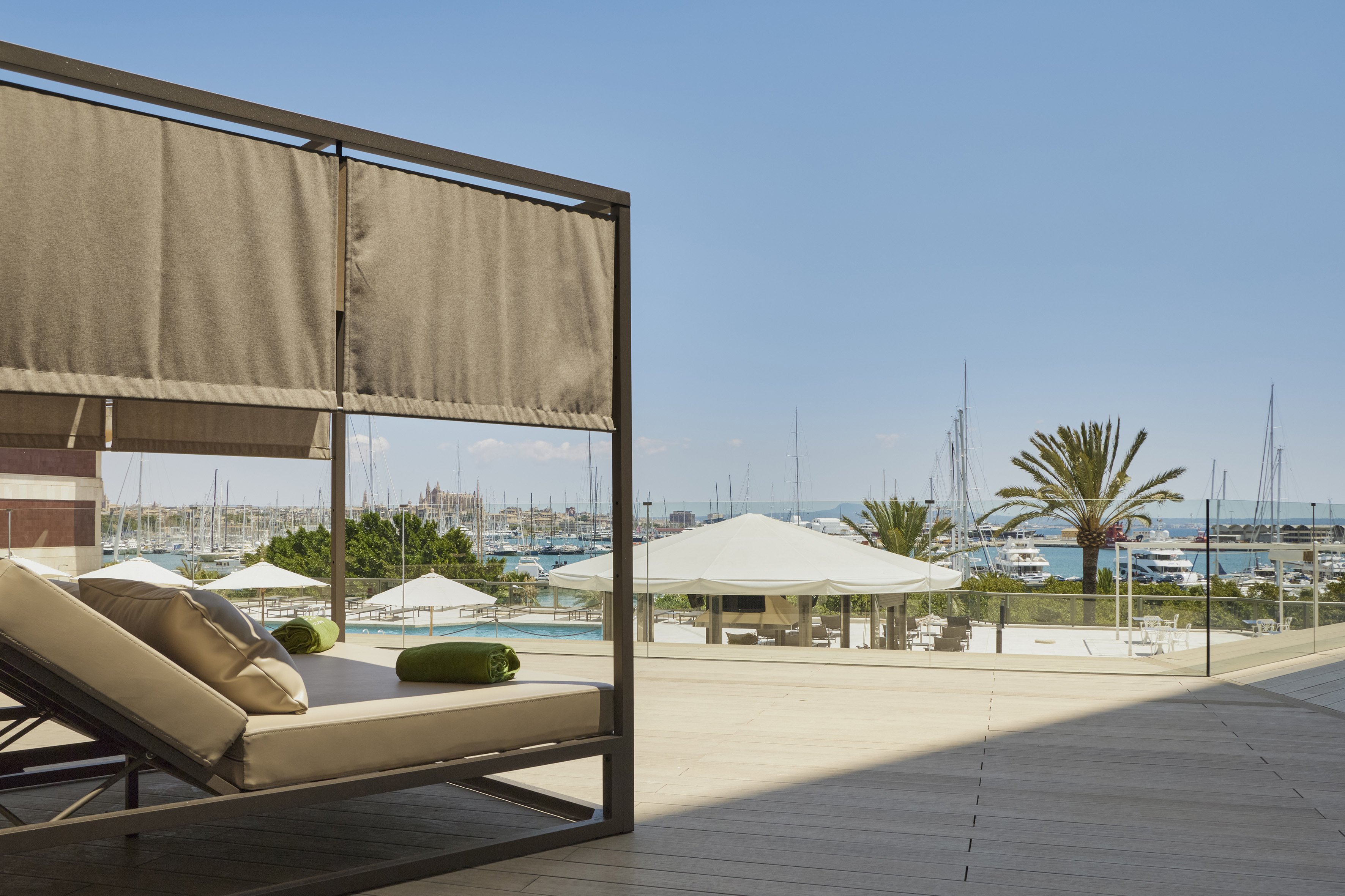 Luxury hotel terrace with daybed, marina views, yachts, and Palma Cathedral.