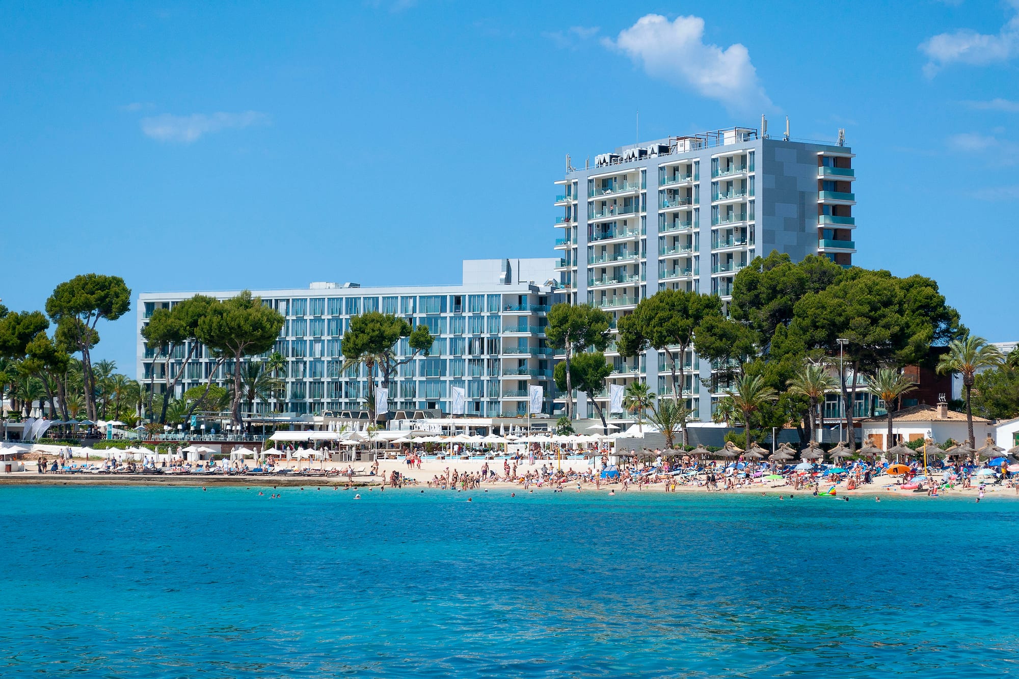 Modern beachfront resort, busy sandy beach, clear blue ocean.