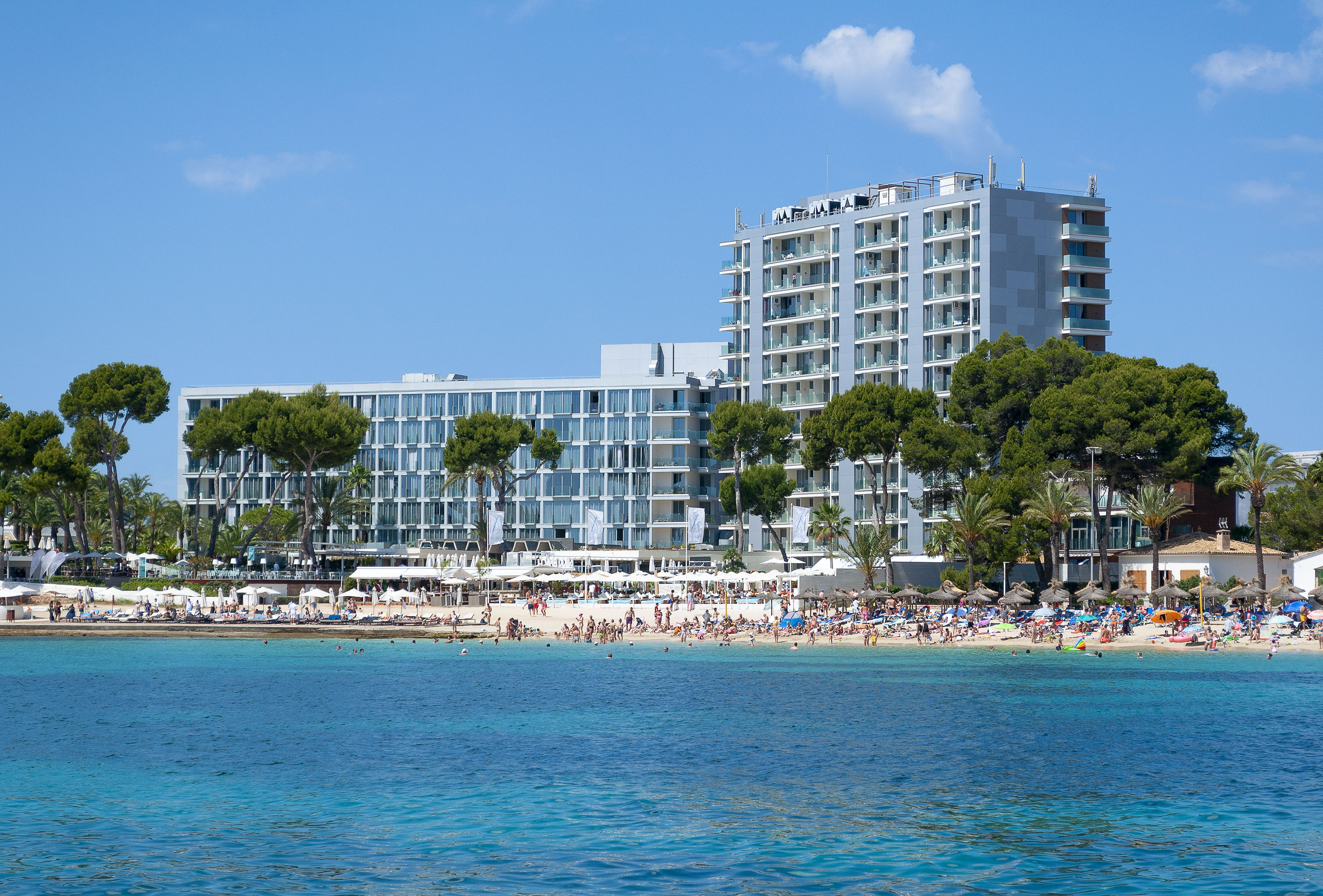 Modern beachfront resort, busy sandy beach, clear blue ocean.