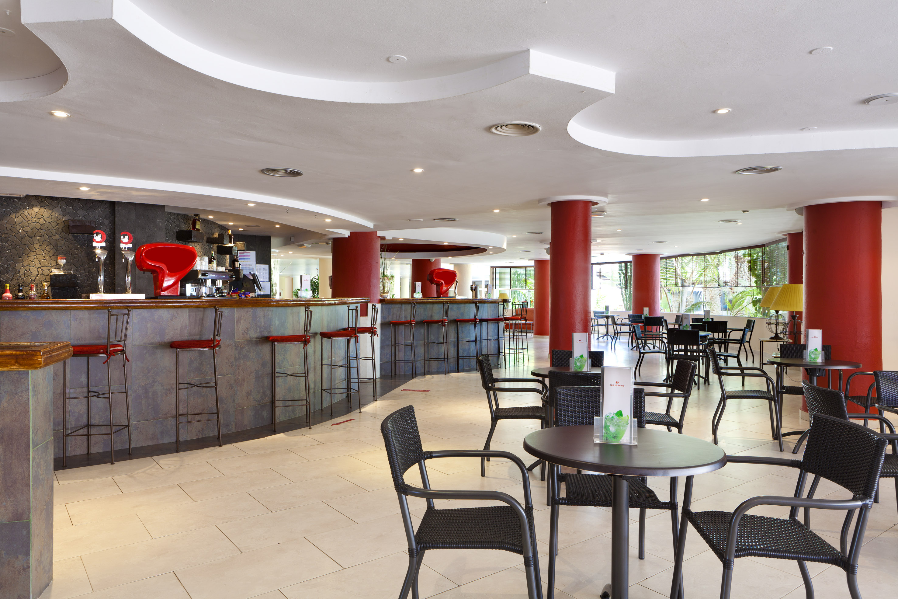 Hotel bar lounge with a long counter, red stools, and various seating areas.