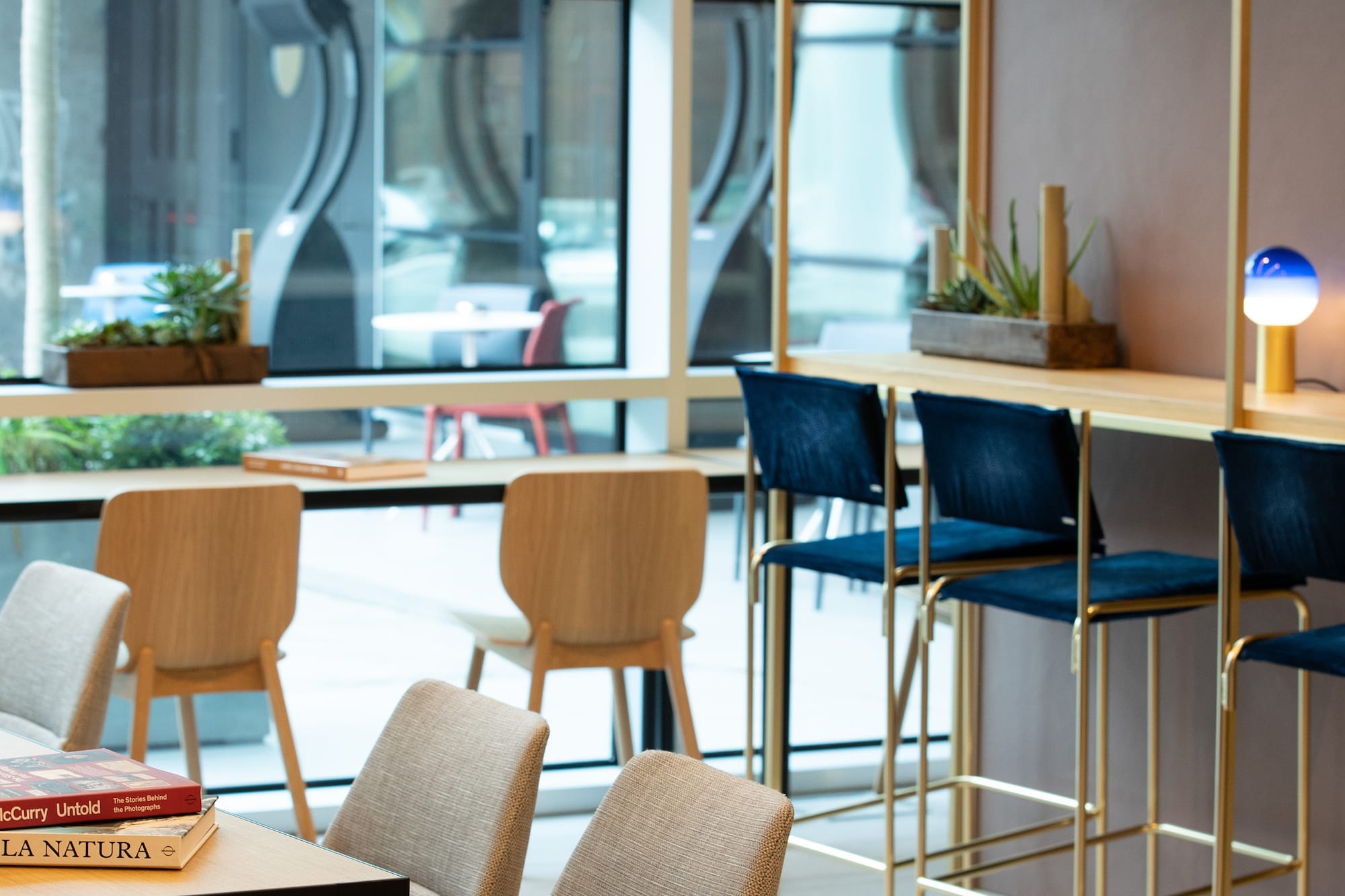 Modern lounge with varied seating, high tables, plants, and window views.