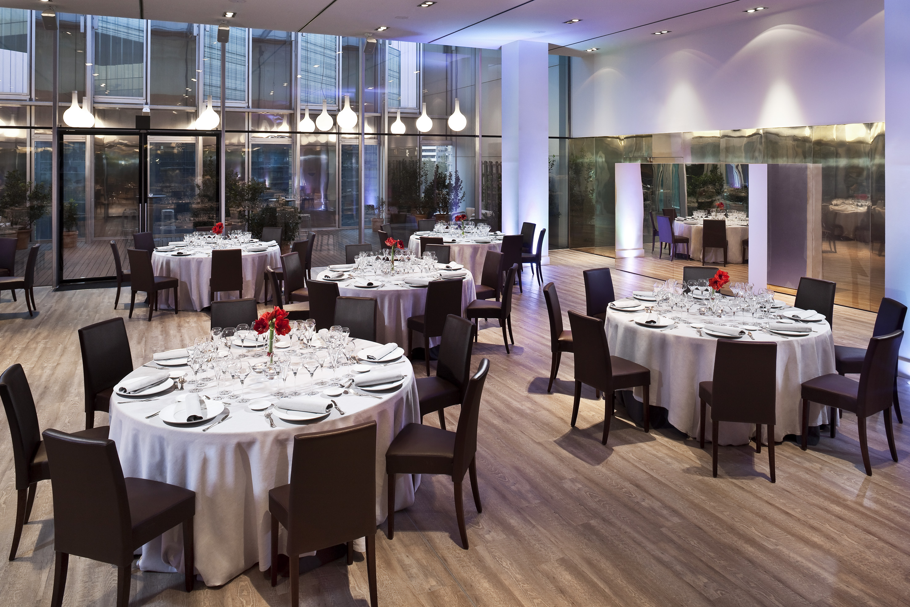 Elegant modern banquet hall with round dining tables, dark chairs, and glass windows.