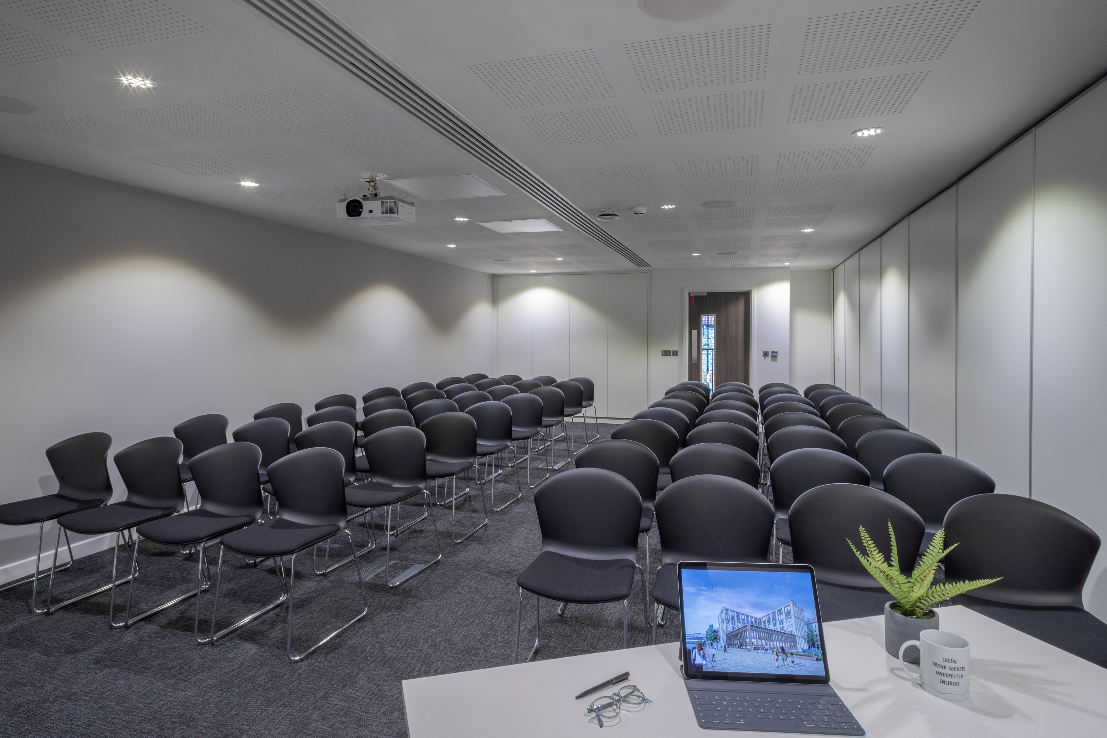 Modern empty conference room with rows of chairs, projector, and tablet.