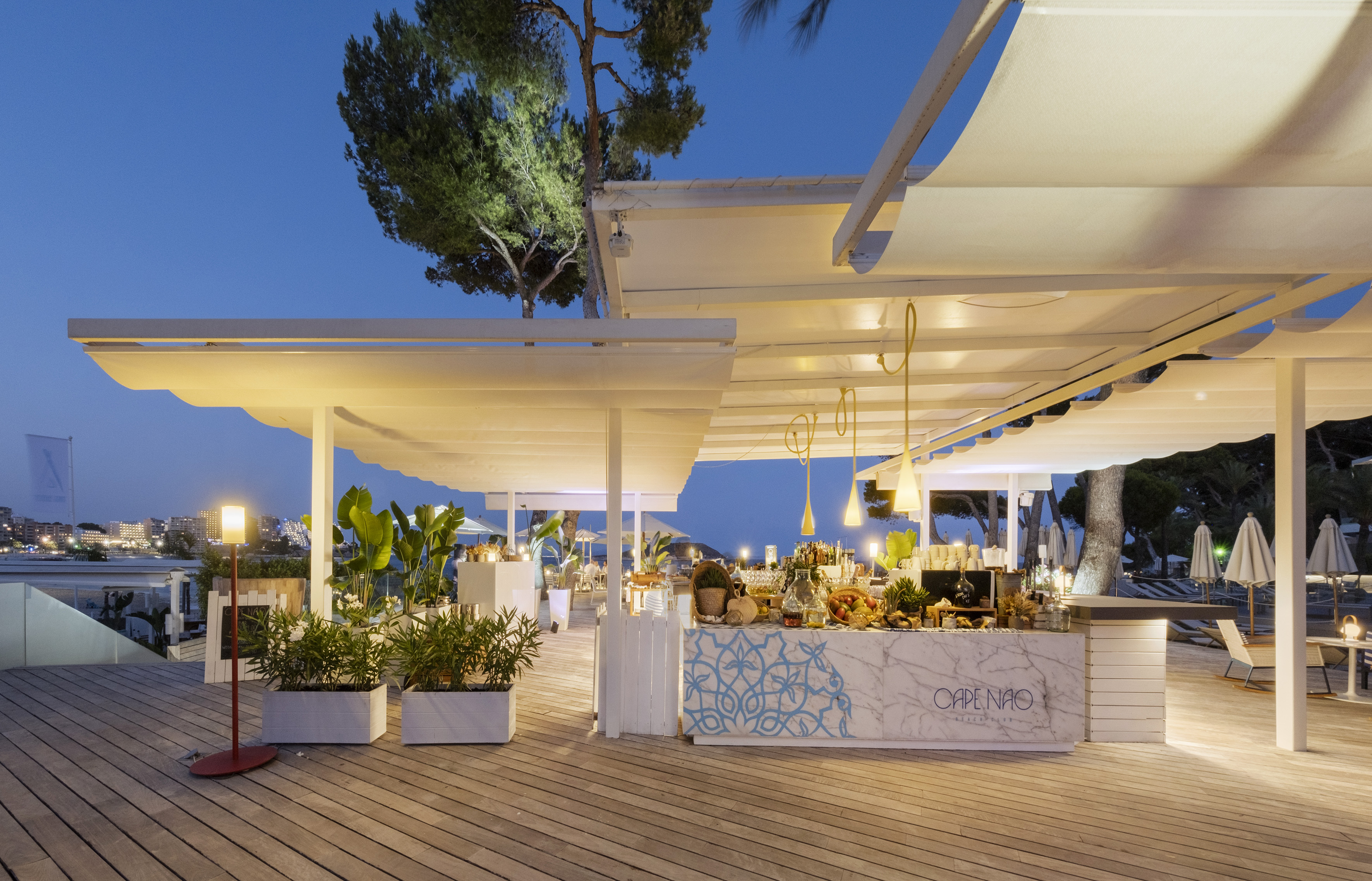CAPE NAO outdoor bar at dusk with white awnings, wooden deck, resort.