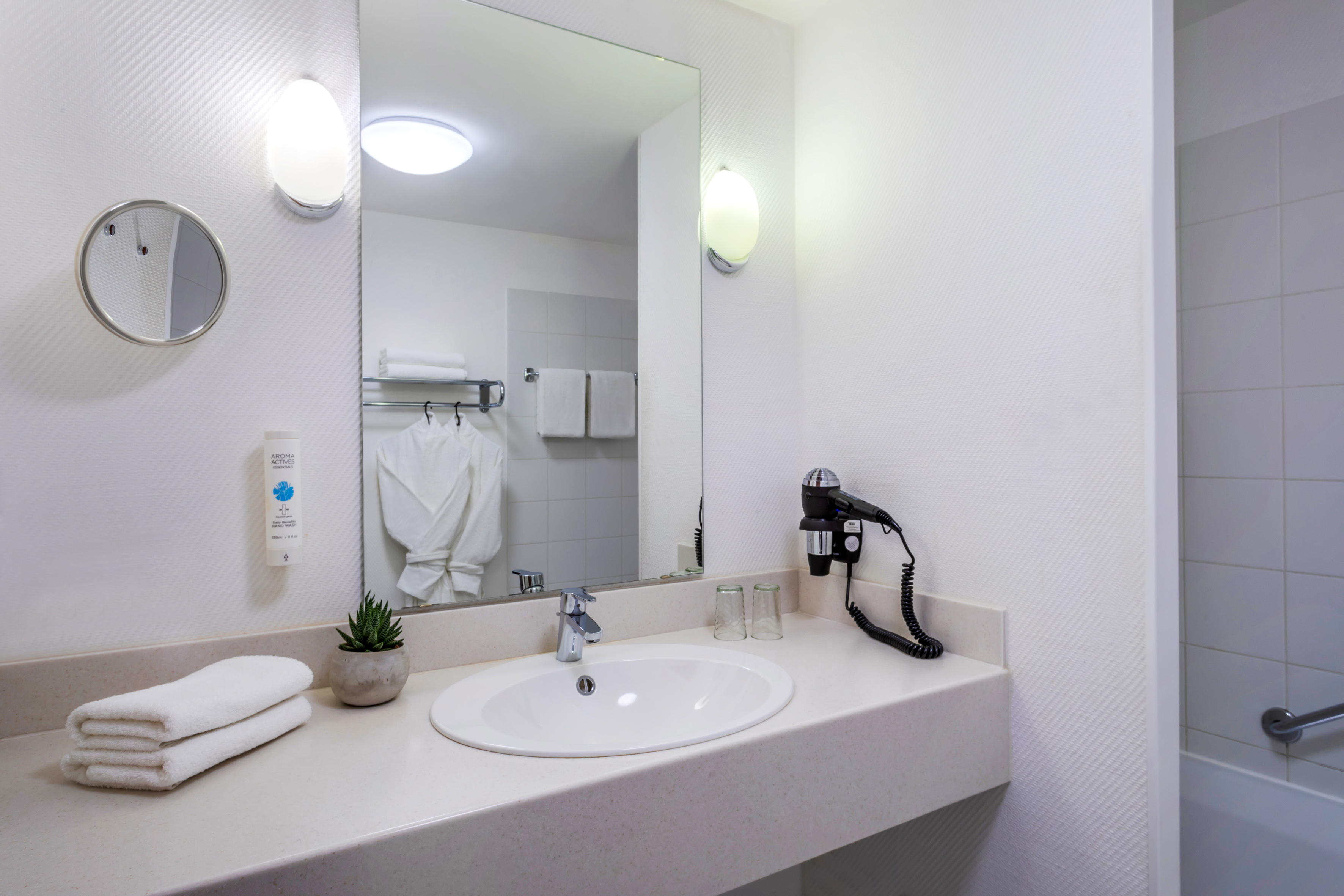 Clean hotel bathroom vanity with white sink, large mirror, fresh towels, hairdryer.