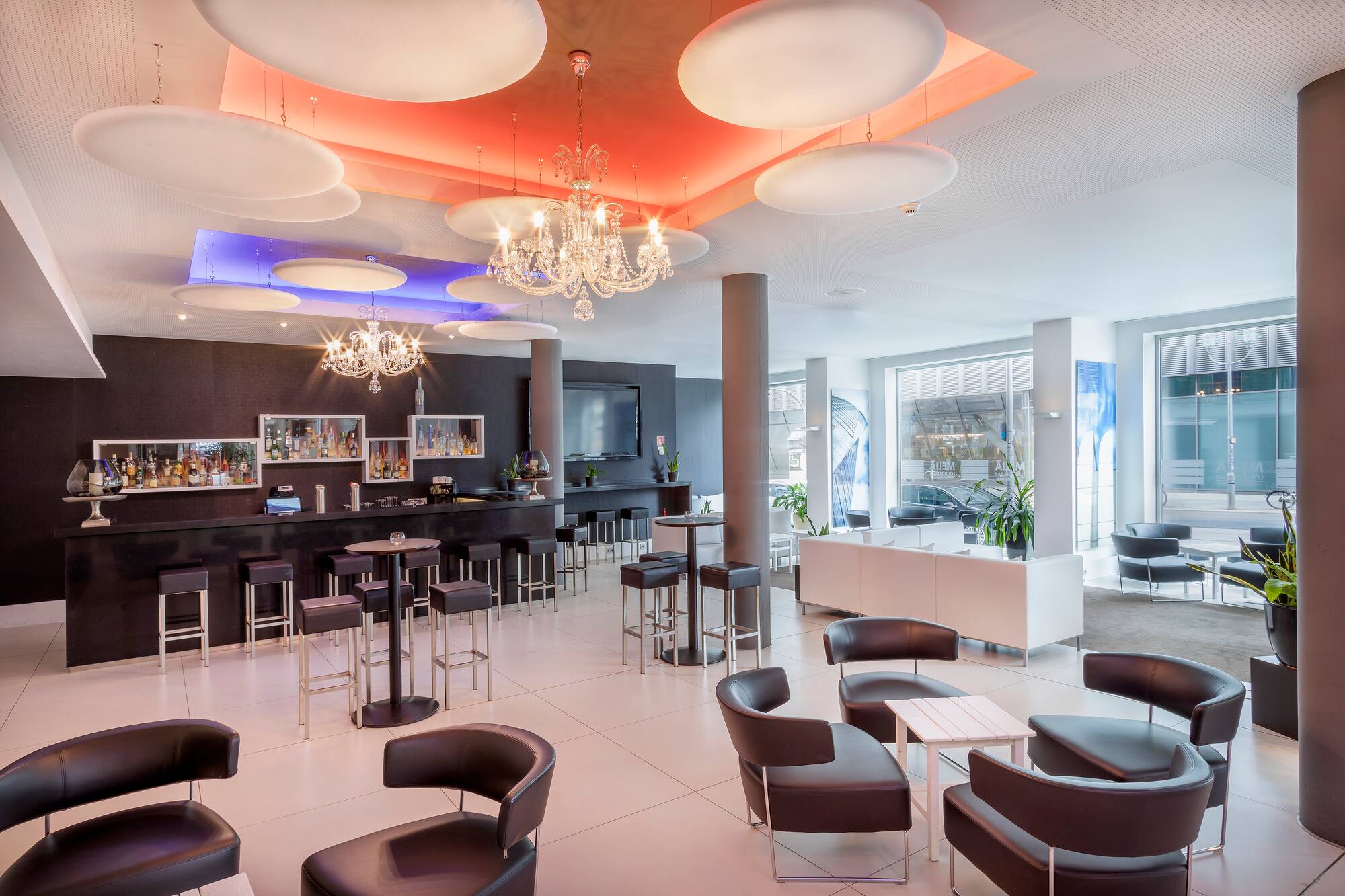 Modern hotel bar lounge with dark counter, chandeliers, and contemporary seating.