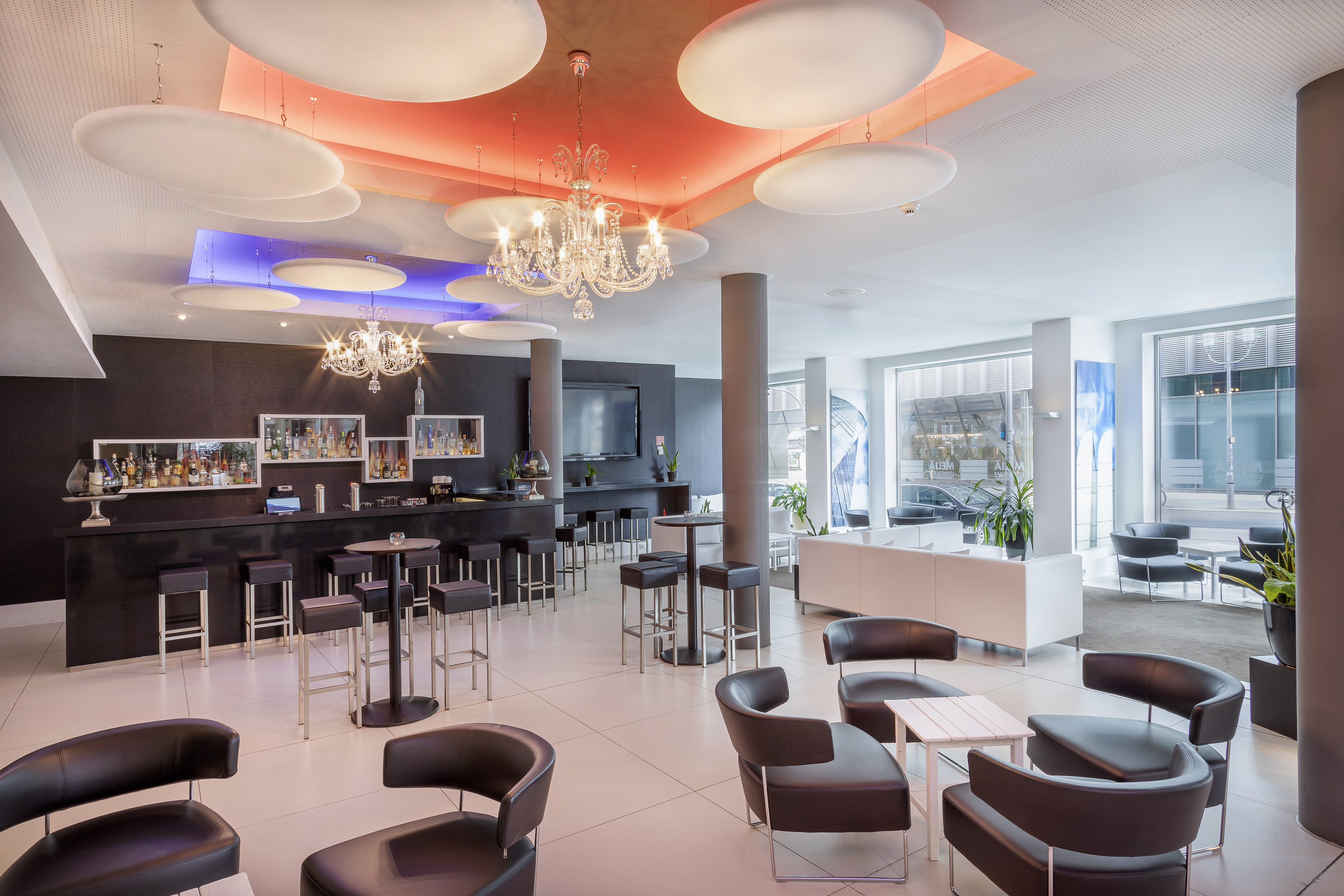 Modern hotel bar lounge with dark counter, chandeliers, and contemporary seating.