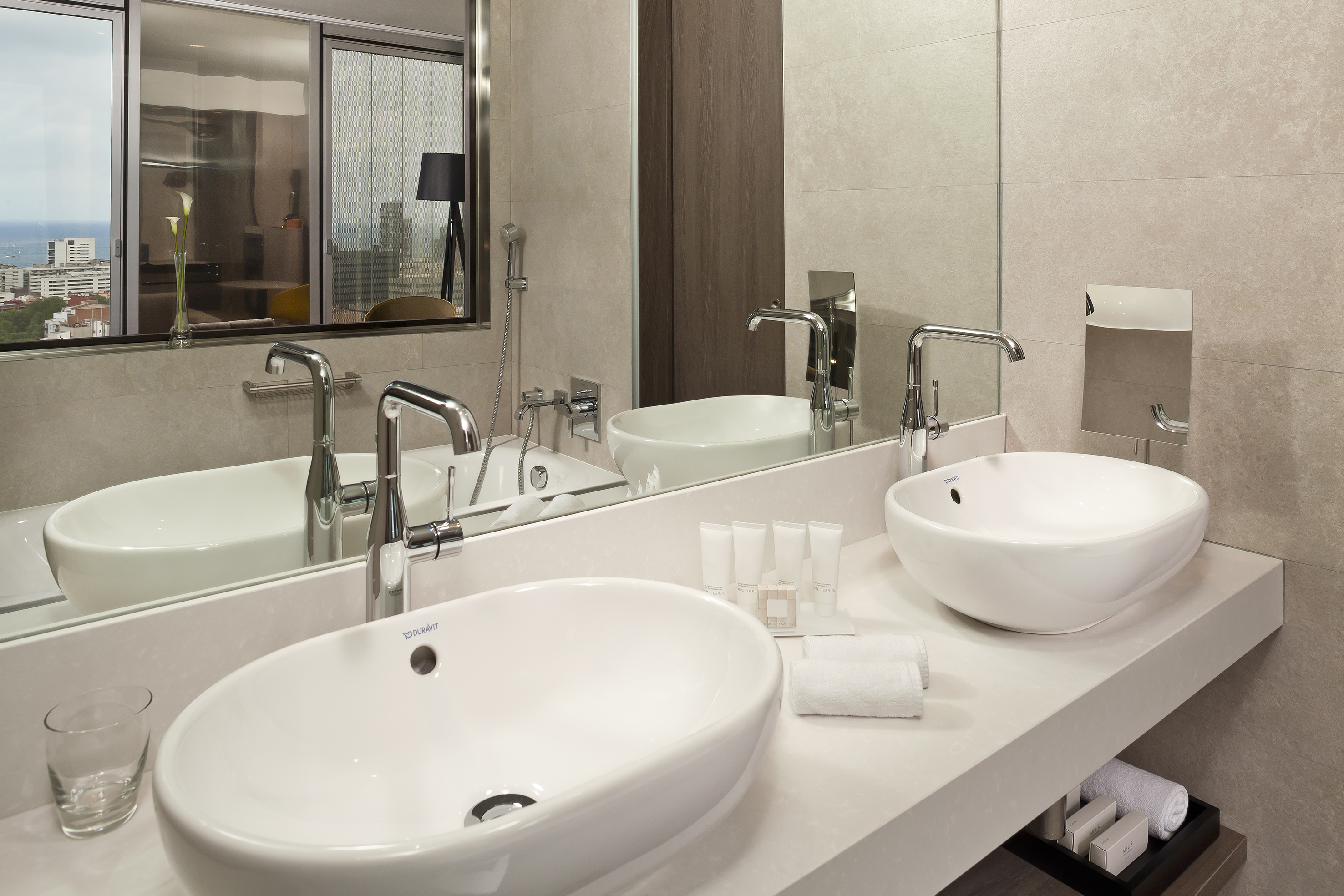 Modern double sink bathroom with chrome faucets and city view window.