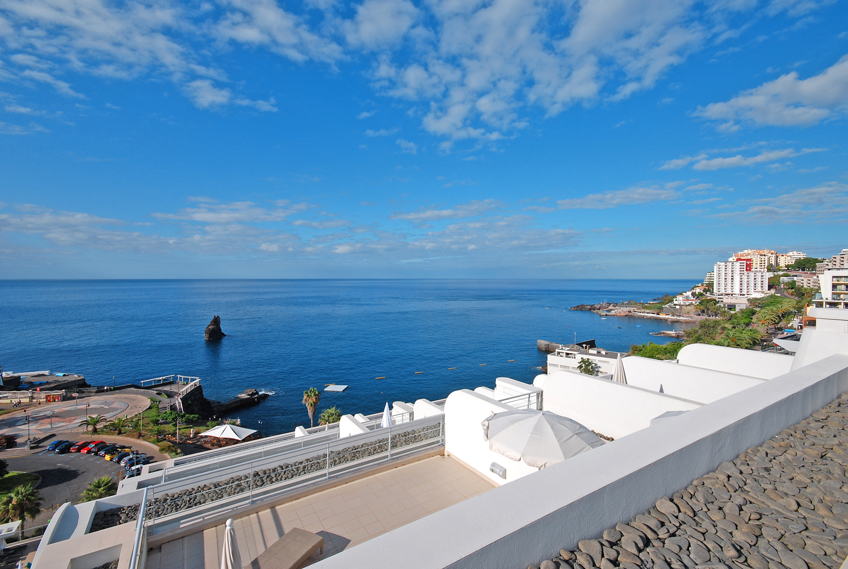 Panoramic ocean view from a hotel balcony over a coastal town and sea stack.