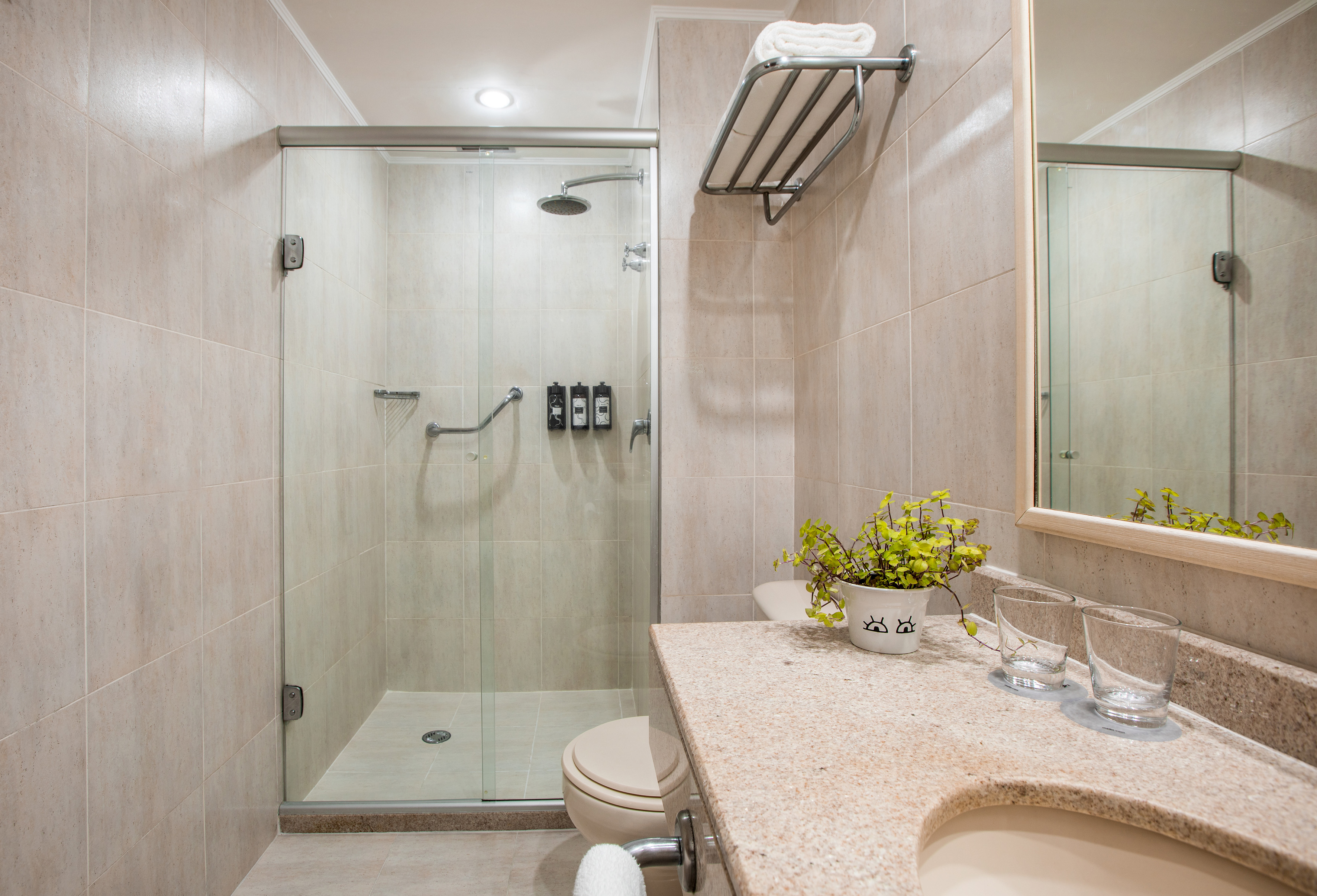 Clean hotel bathroom with glass enclosed shower, beige tiles, and vanity.