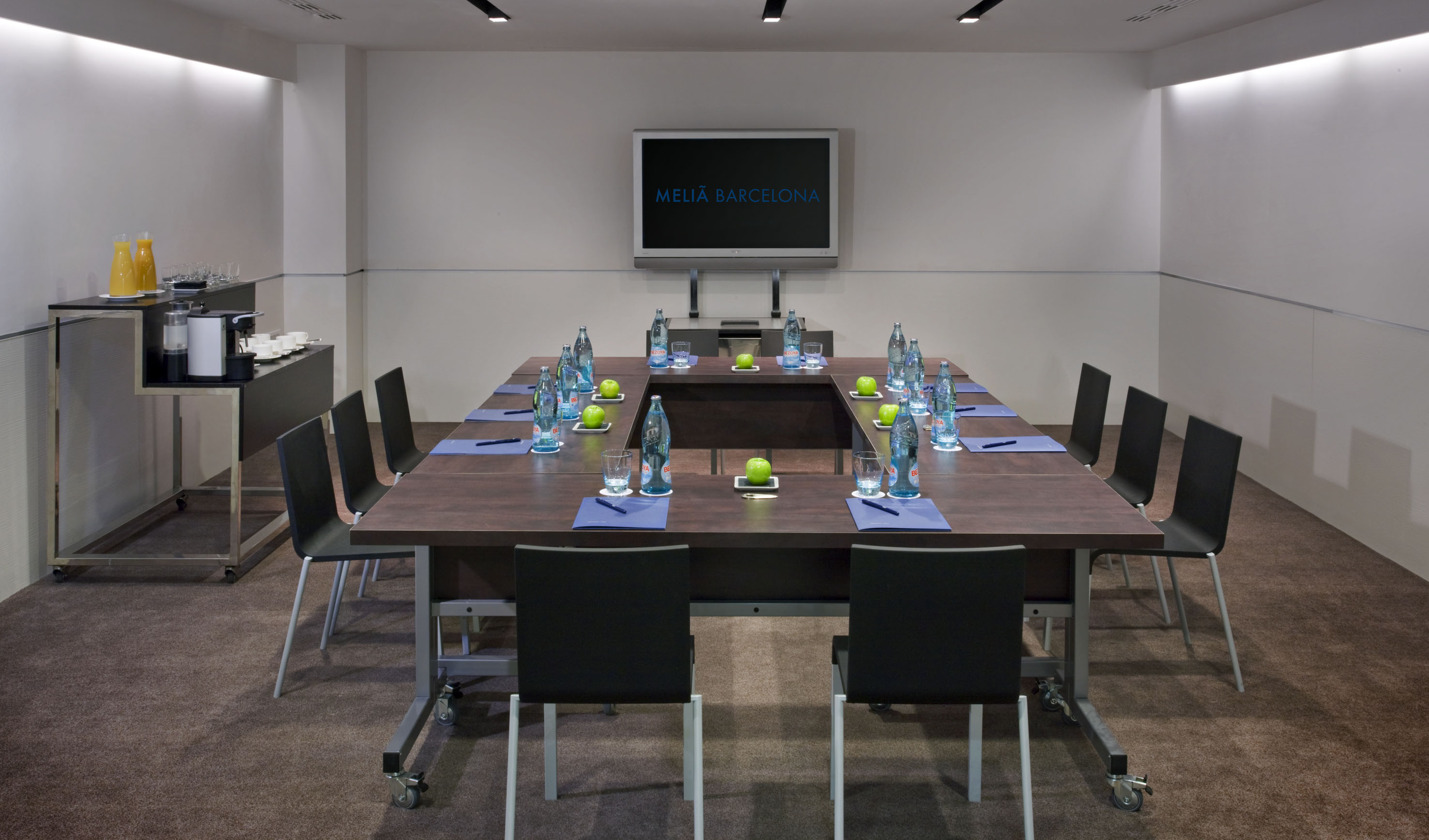 Meliá Barcelona meeting room with U-shaped table, display screen, and refreshments.